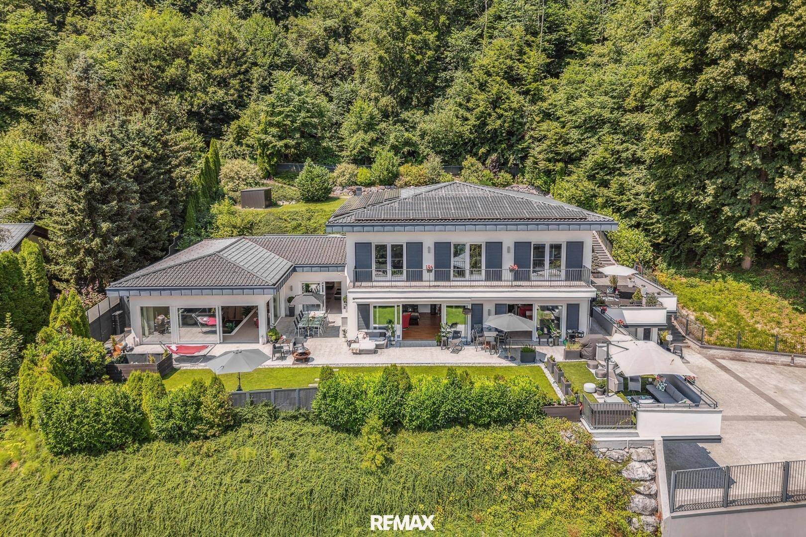 Luftaufnahme des modernen Hauses mit weitläufigen Terrassen und umgeben von grüner Natur.
