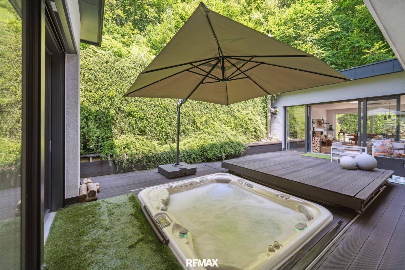Entspannungsbereich im Freien mit Whirlpool und Holzterrasse, umgeben von üppigem Grün.