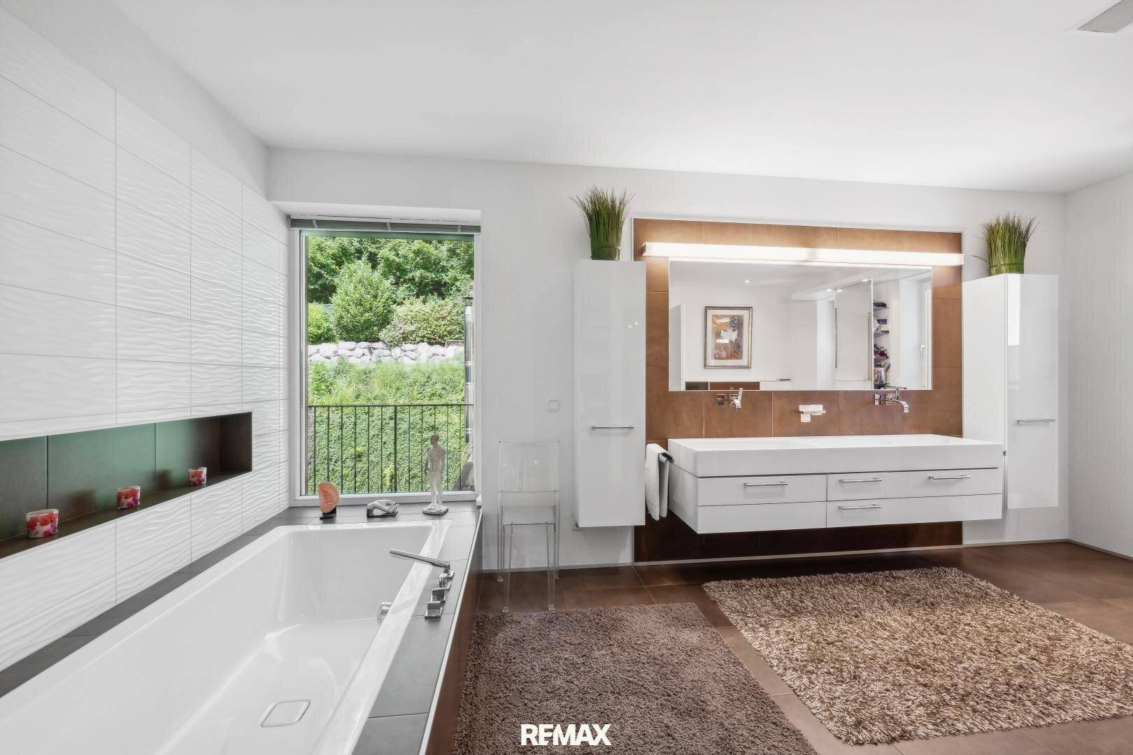 Modernes Badezimmer mit großer Badewanne, Doppelwaschbecken und Fenster mit Blick ins Grüne.