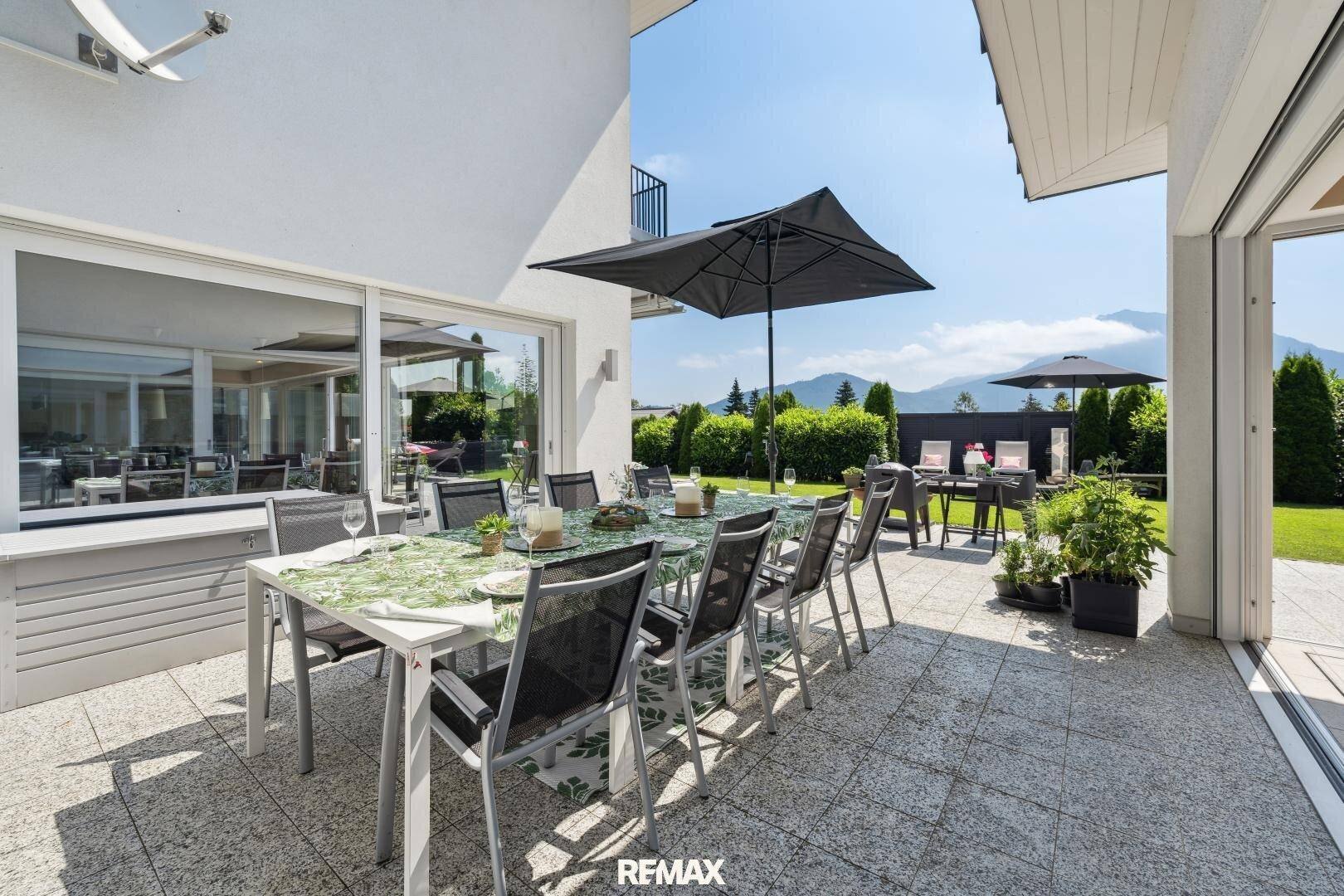 Große geflieste Terrasse mit Esstisch, Sonnenschirm und weitem Blick auf die Berge.
