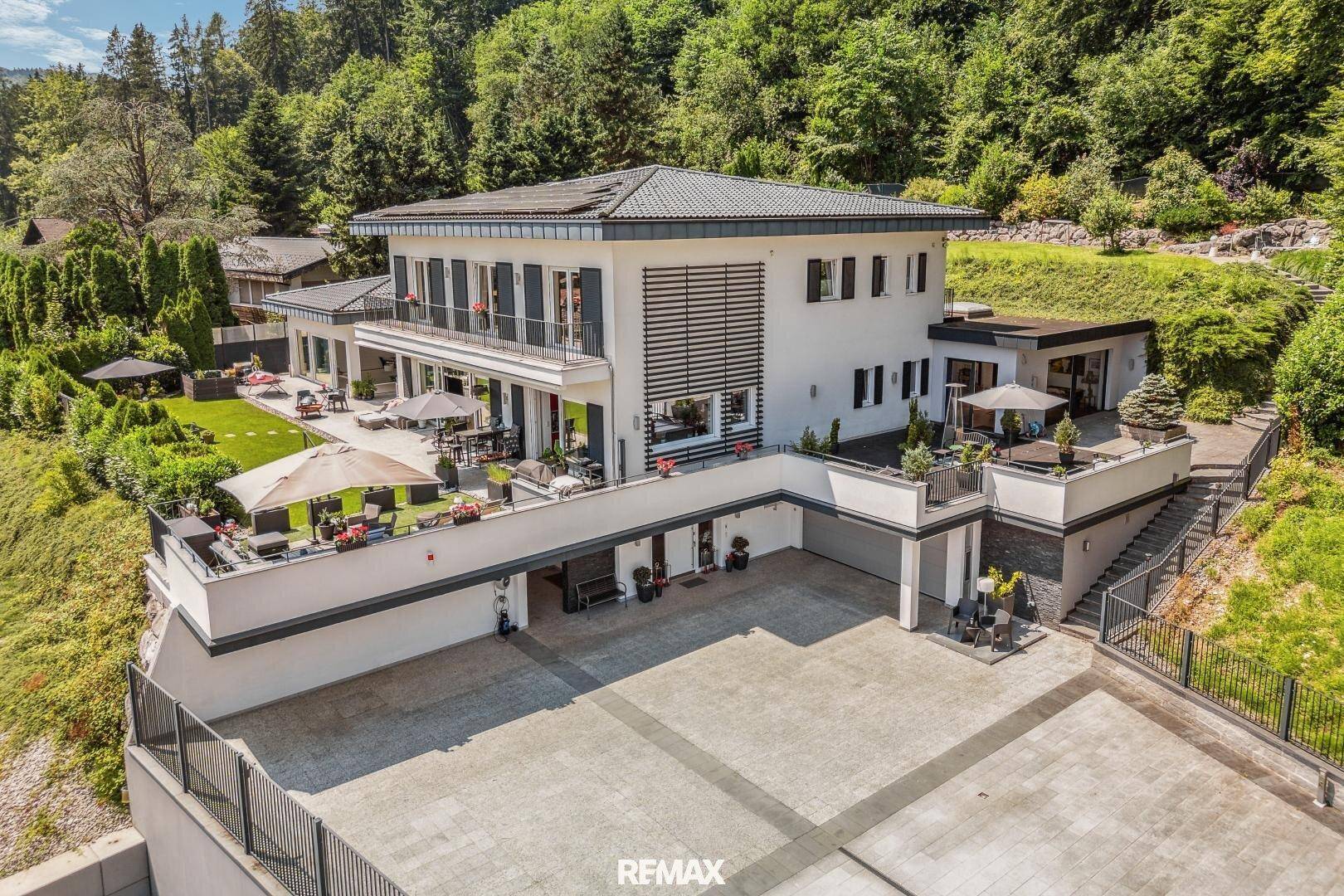 Großzügiges Anwesen mit moderner Architektur, mehreren Terrassen und einer geräumigen Garagenzufahrt.