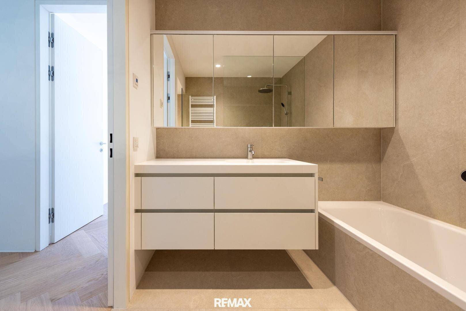 Modernes Badezimmer mit elegantem Waschtisch, Spiegelschrank und integrierter Badewanne.
