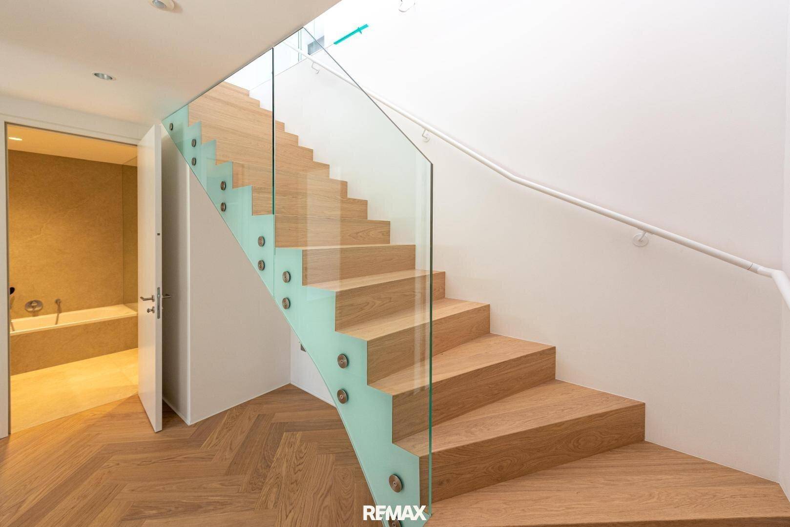 Elegante Holztreppe mit Glasgeländer und Blick auf ein modernes Badezimmer.