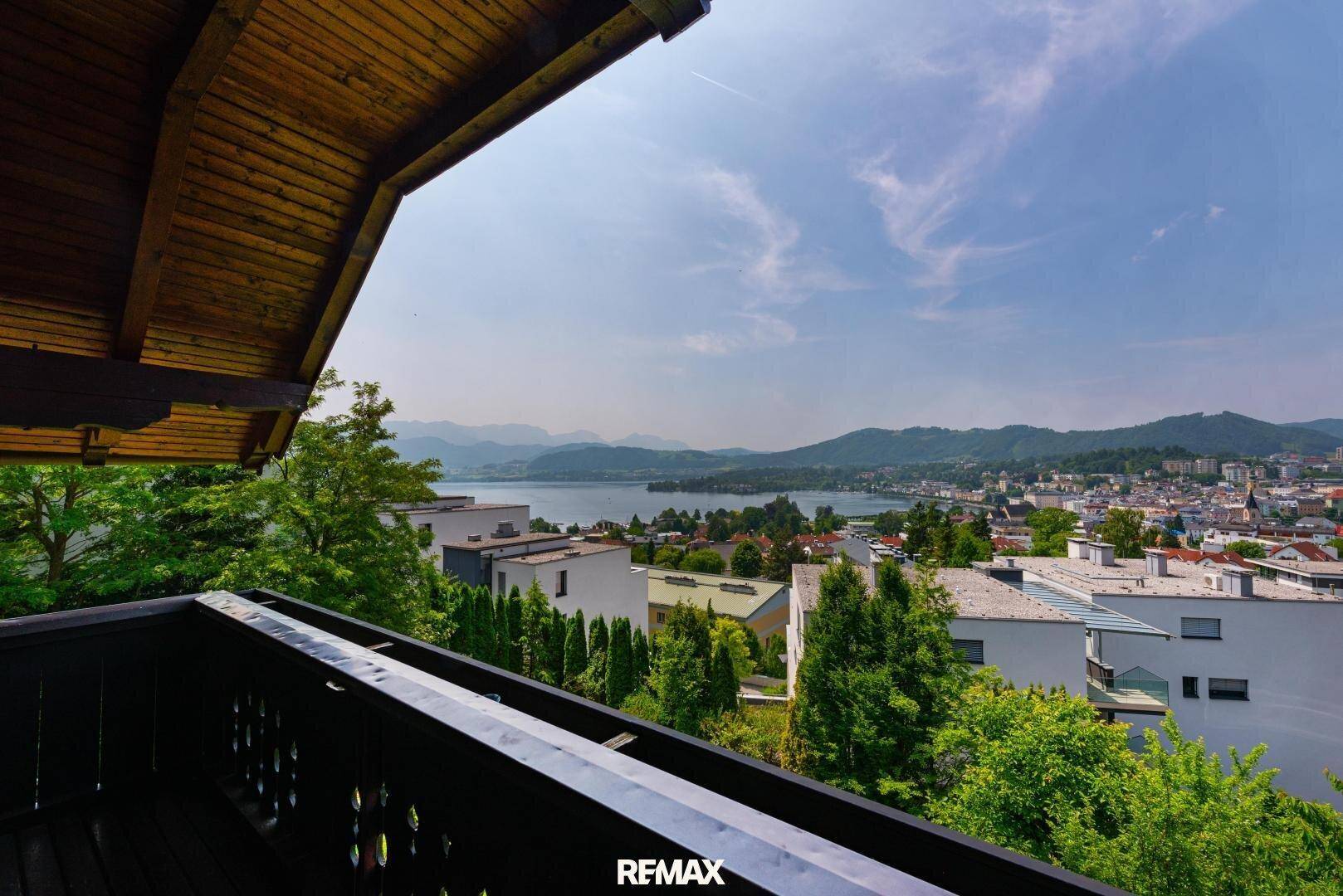 Balkon mit Holzbalken und Geländer, bietet einen weiten Blick auf den See und die umliegende Berglandschaft.