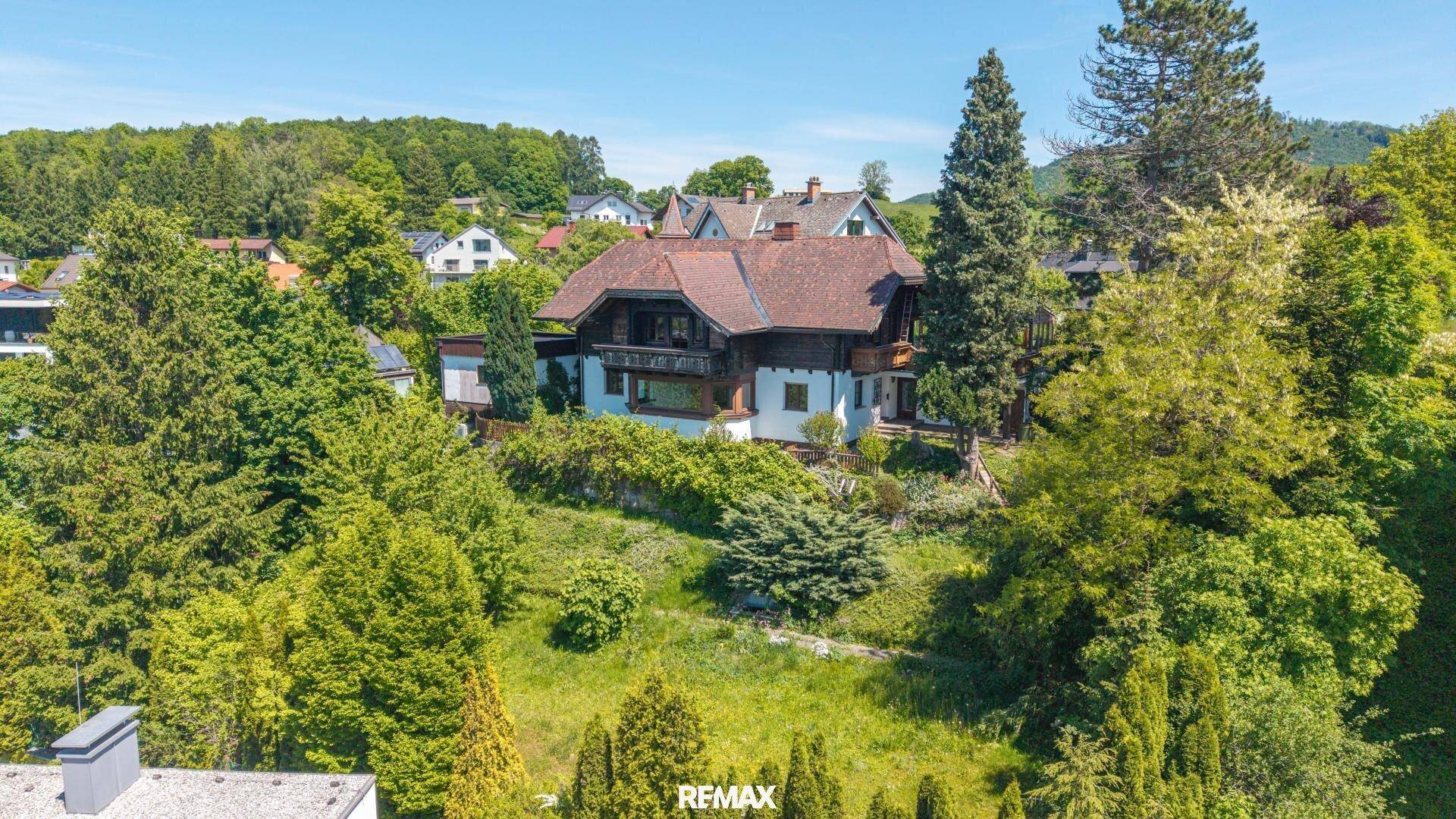 Traditionelles Haus in Hanglage, umgeben von viel Grün und Bäumen, mit Blick auf die Nachbarschaft.