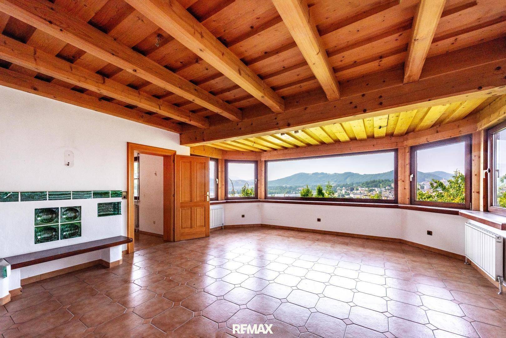 Heller Wohnraum mit Holzbalkendecke, Fliesenboden und großen Panoramafenstern mit weitem Ausblick.
