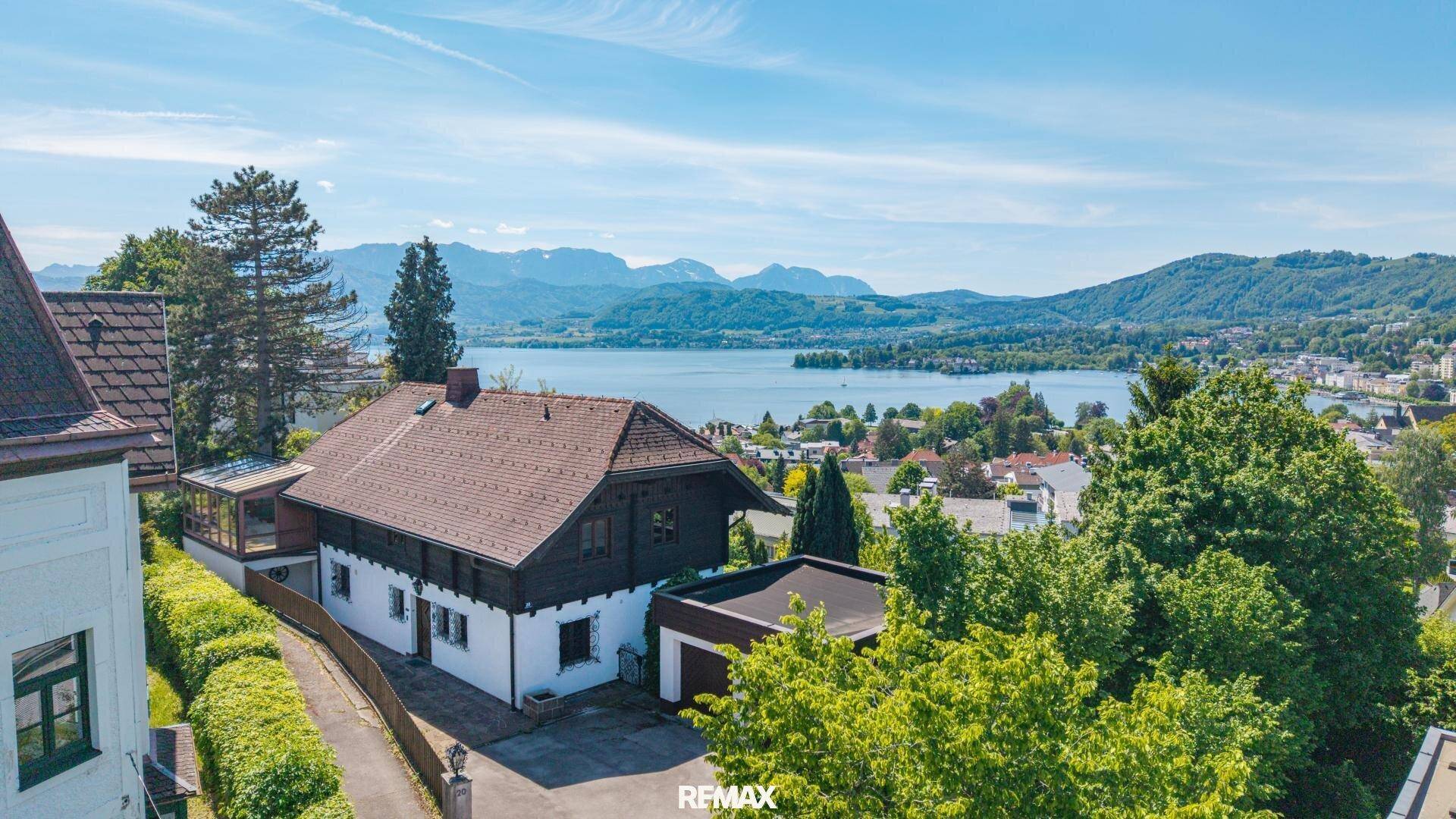 Traditionelles Haus mit Satteldach und Garage, umgeben von viel Grün, mit weitem Blick auf den See und die Berge.