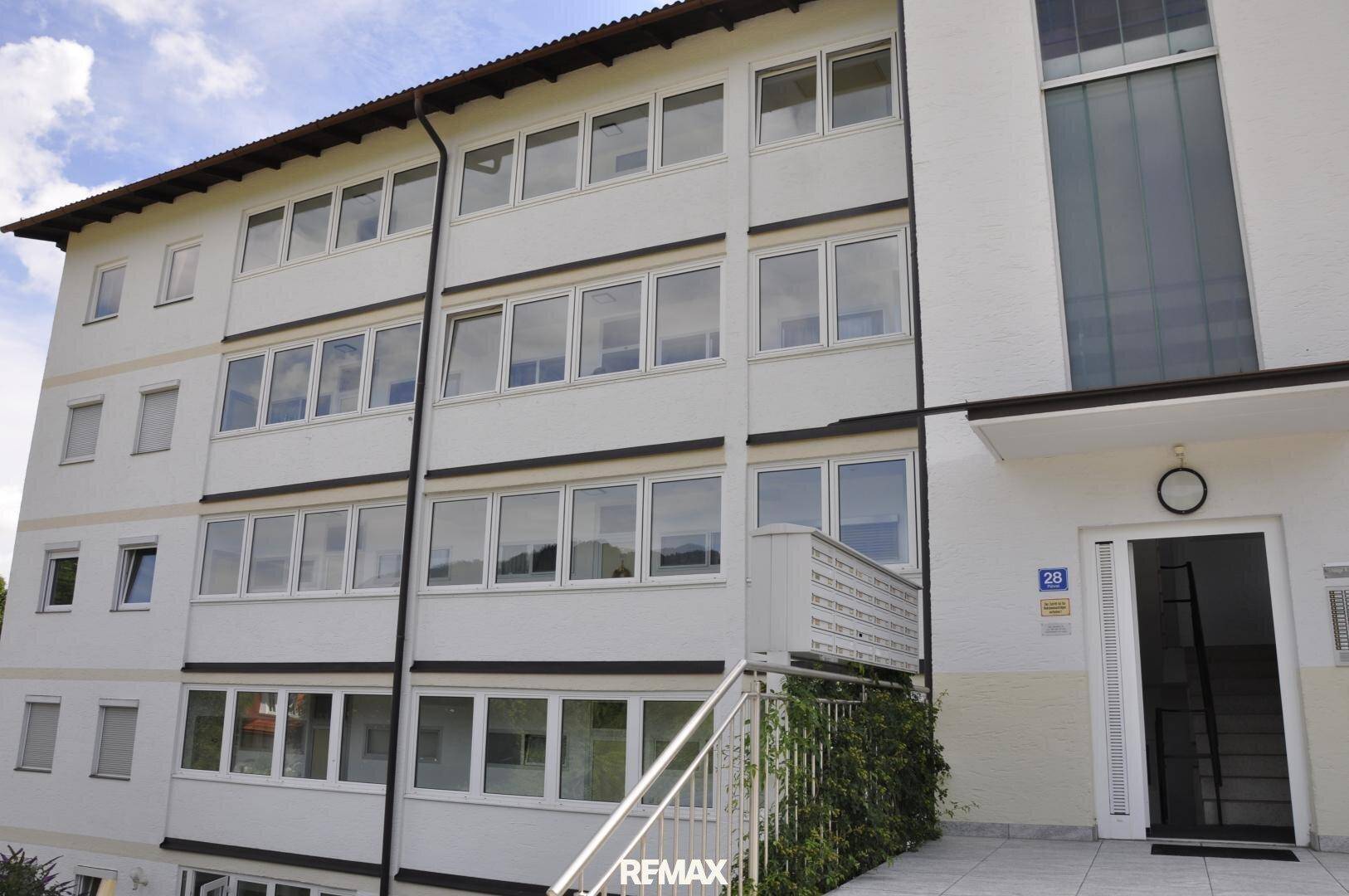 Mehrstöckiges Wohngebäude mit weißer Fassade und vielen Fenstern unter bewölktem Himmel.