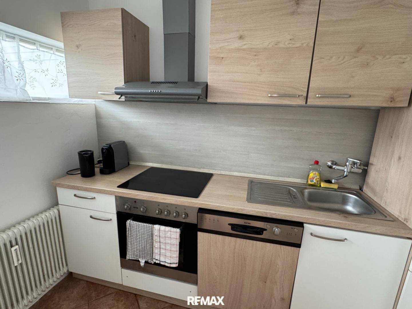 Moderne Einbauküche mit Holzfronten, Kochfeld, Backofen und Spülmaschine.