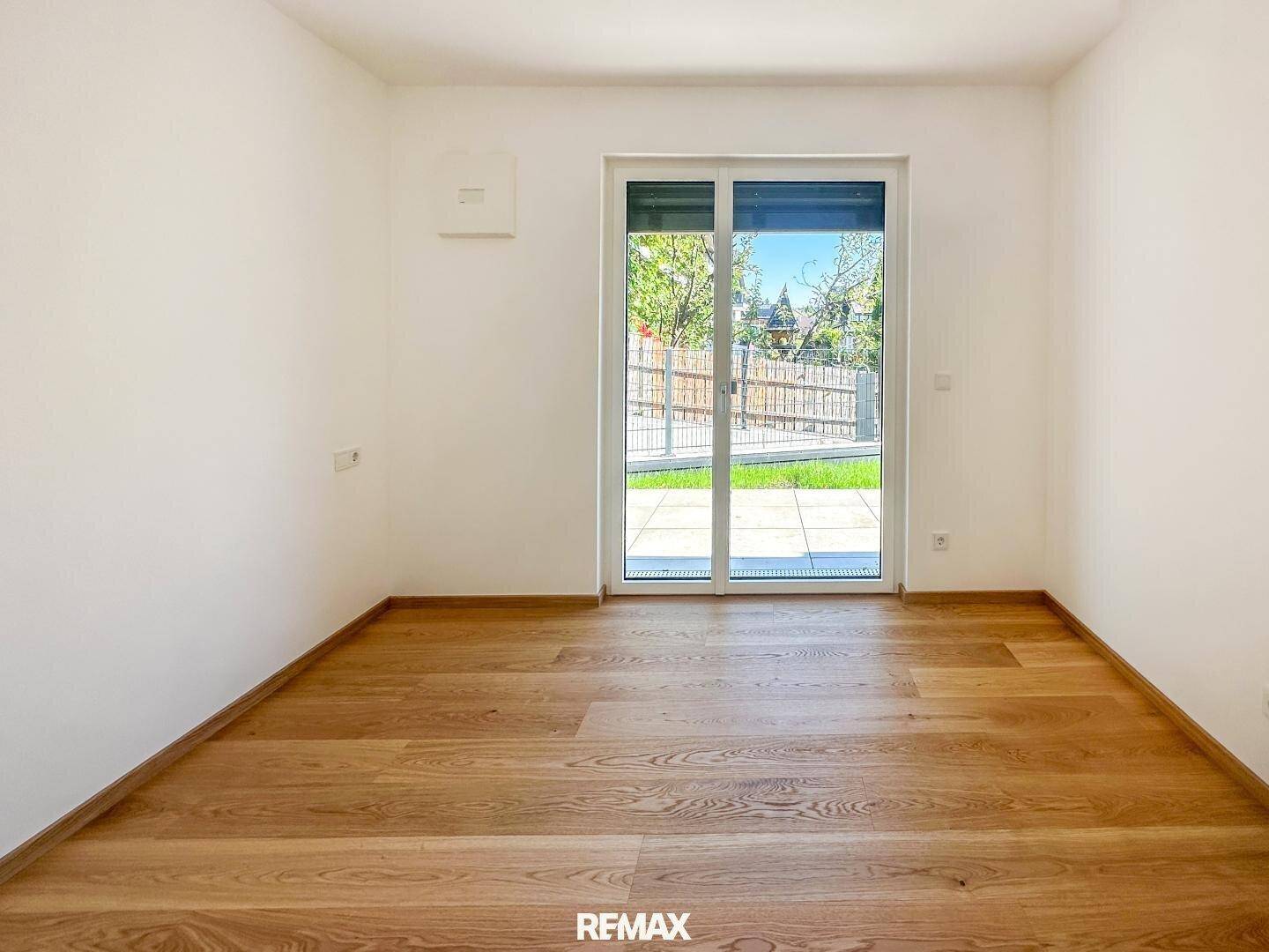 Leeres Zimmer mit Holzboden und Zugang zu einem kleinen Gartenbereich.