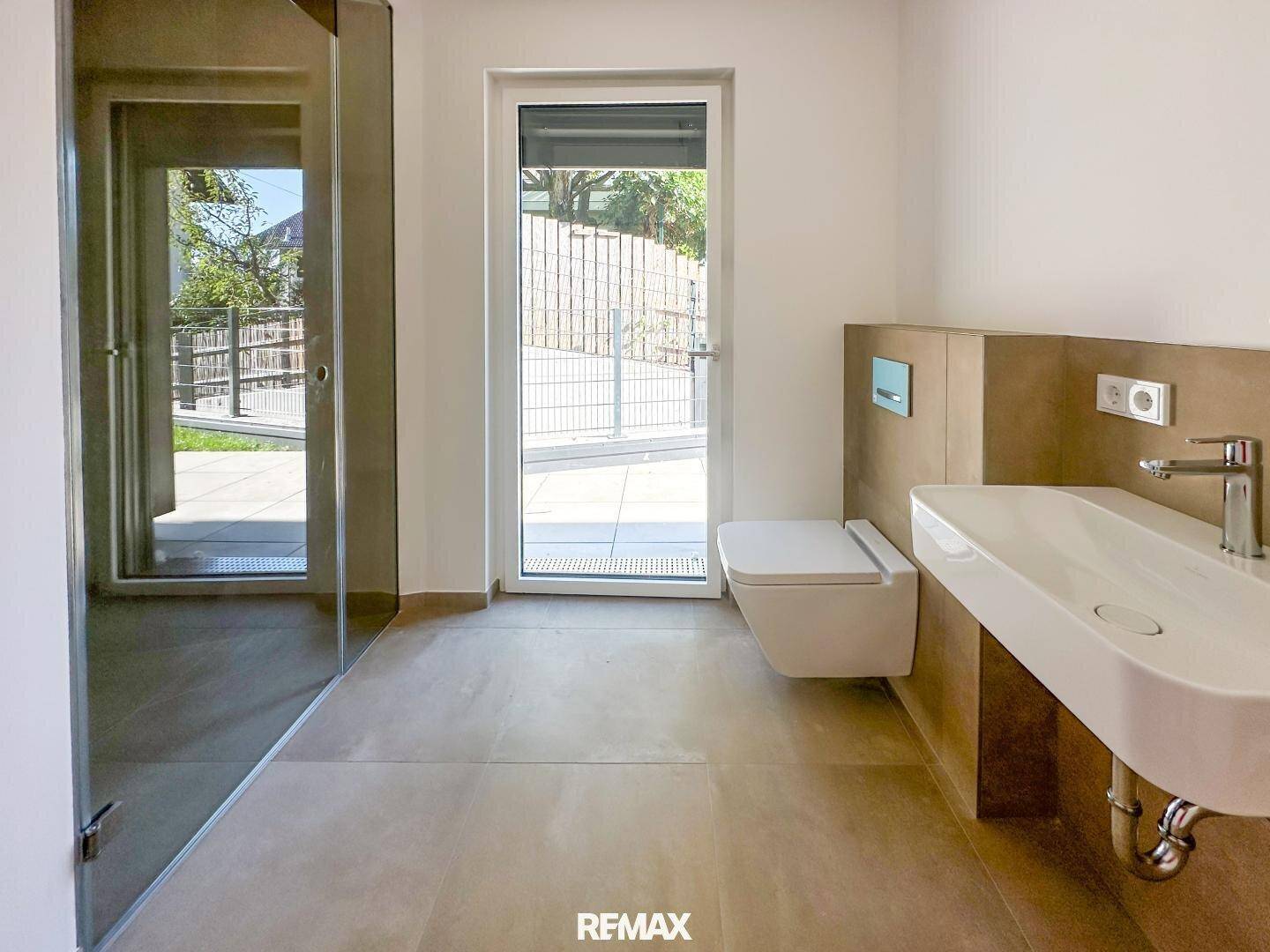 Modernes Badezimmer mit begehbarer Dusche, wandhängendem WC, modernem Waschbecken und direktem Zugang zur Terrasse.