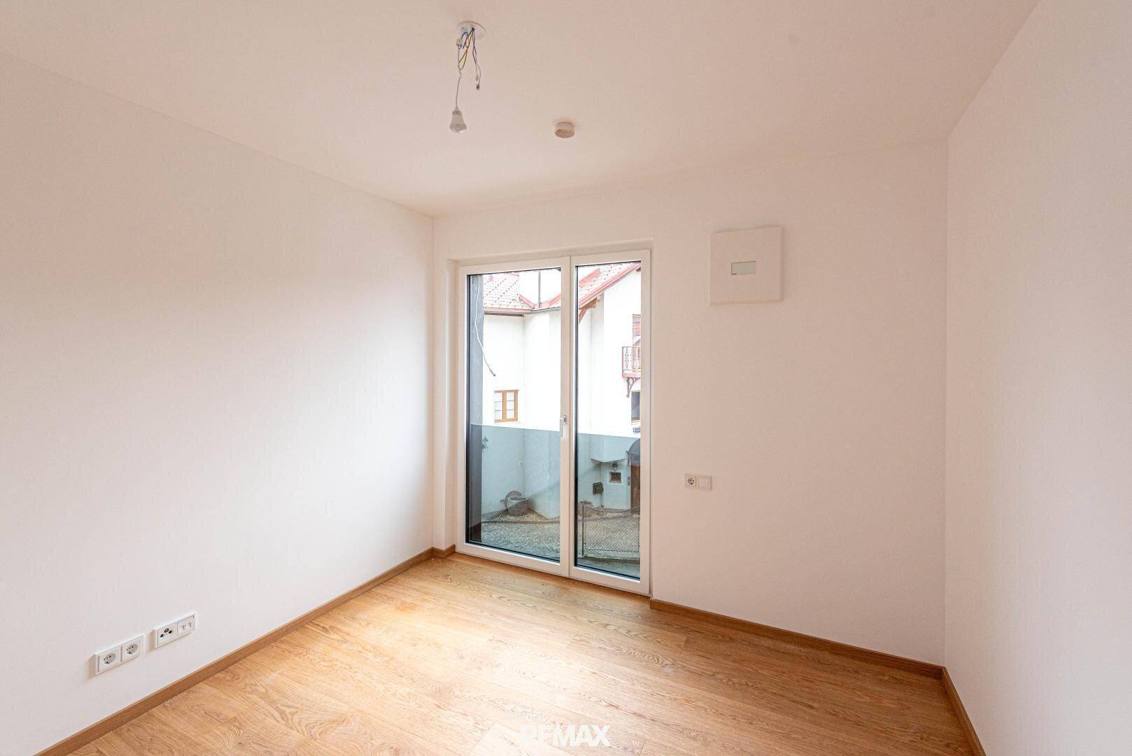 Unmöbliertes Zimmer mit Parkettboden und Zugang zu einem kleinen Außenbereich.