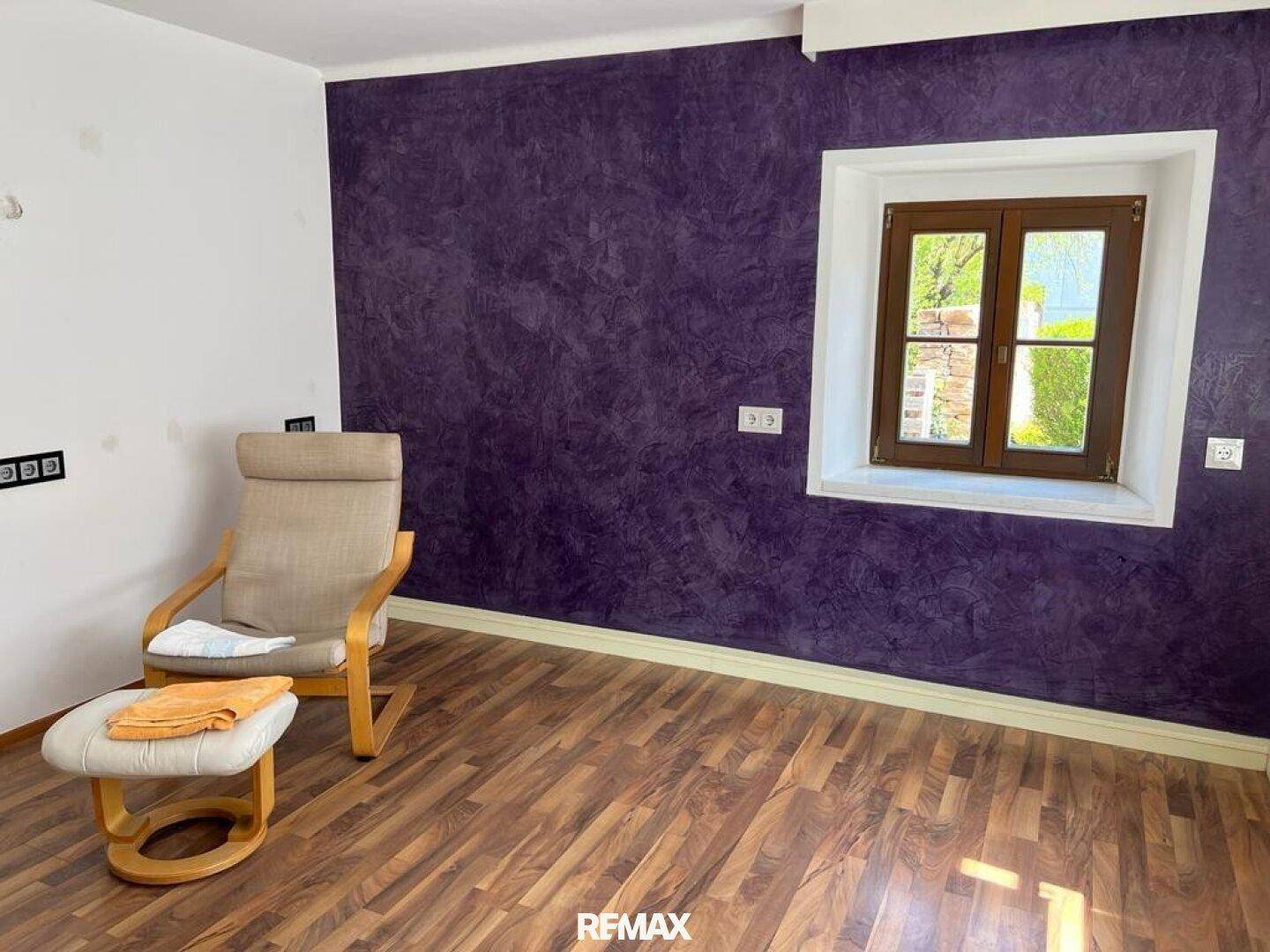 Gemütliches Zimmer mit auffälliger violetter Akzentwand und Holzboden, ideal als Schlaf- oder Arbeitszimmer.