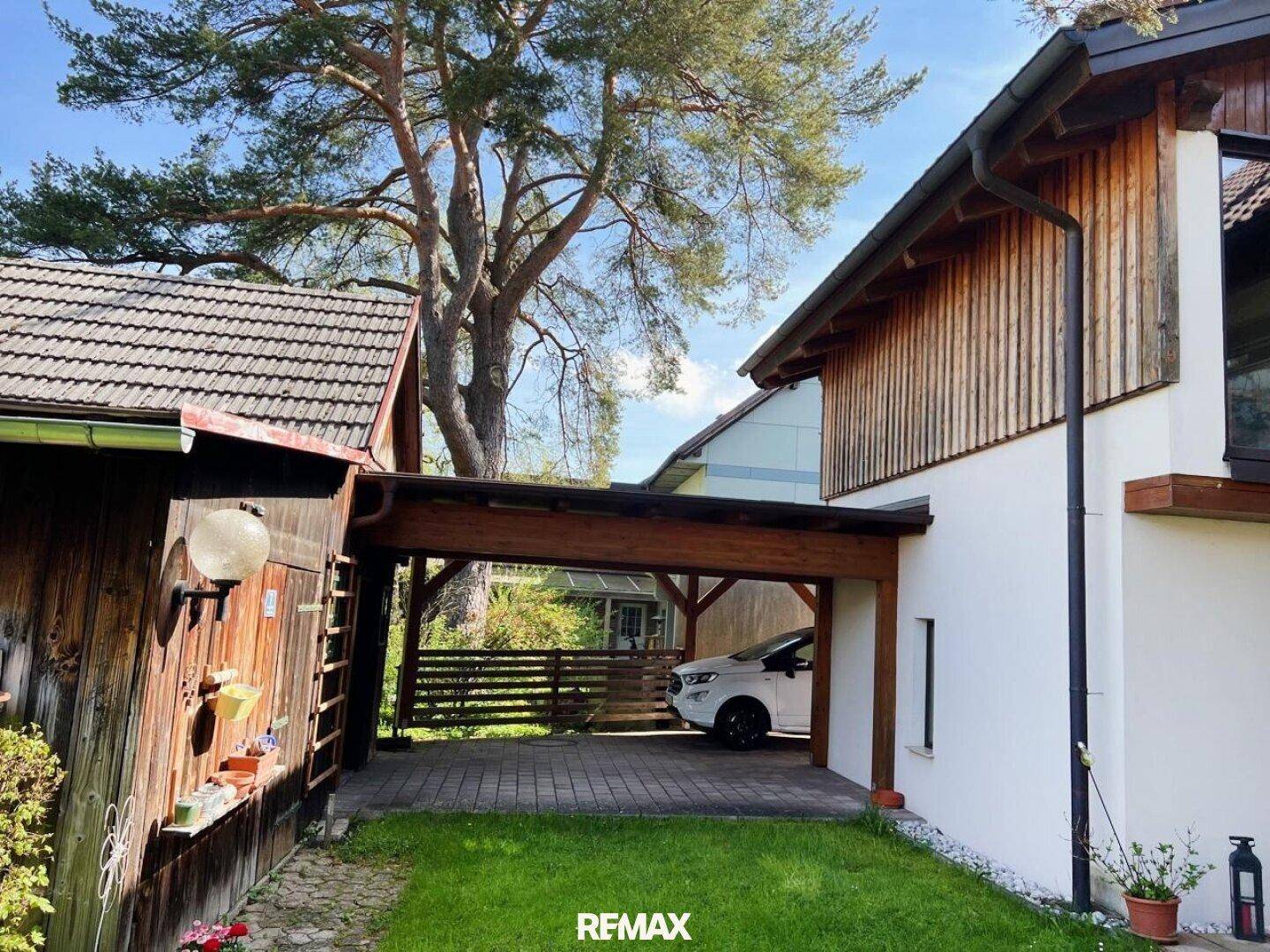 Geräumiger Holzcarport neben dem Haus mit gepflastertem Bereich und Grünfläche.