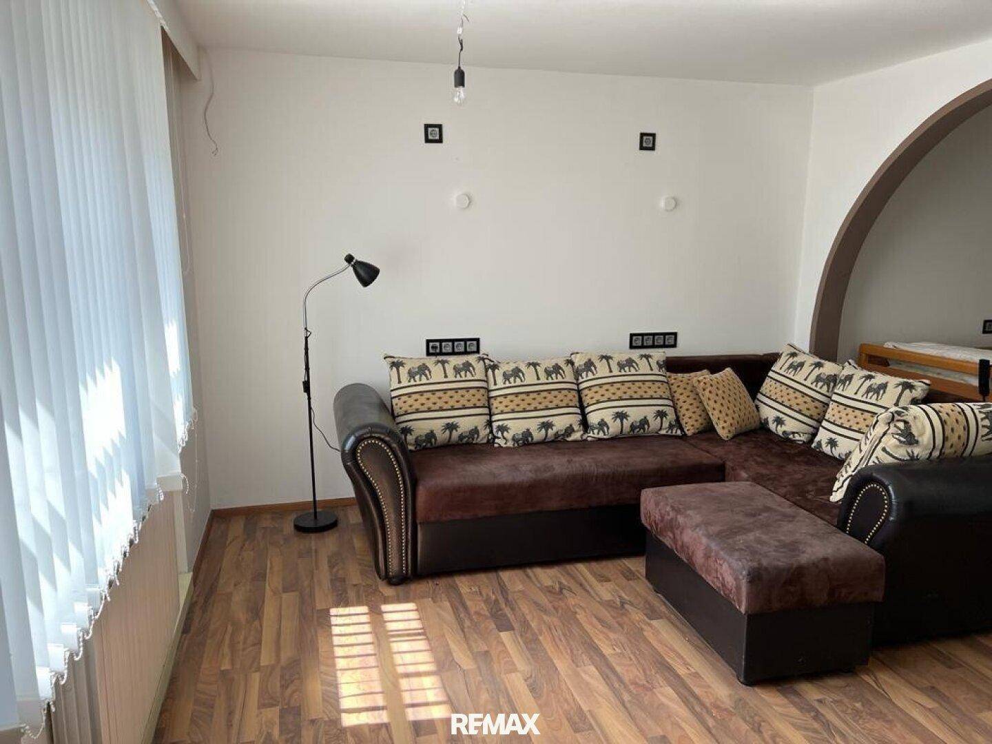 Heller Wohnbereich mit großem L-förmigem Sofa, Holzboden und einem Bogen zum Nebenraum.