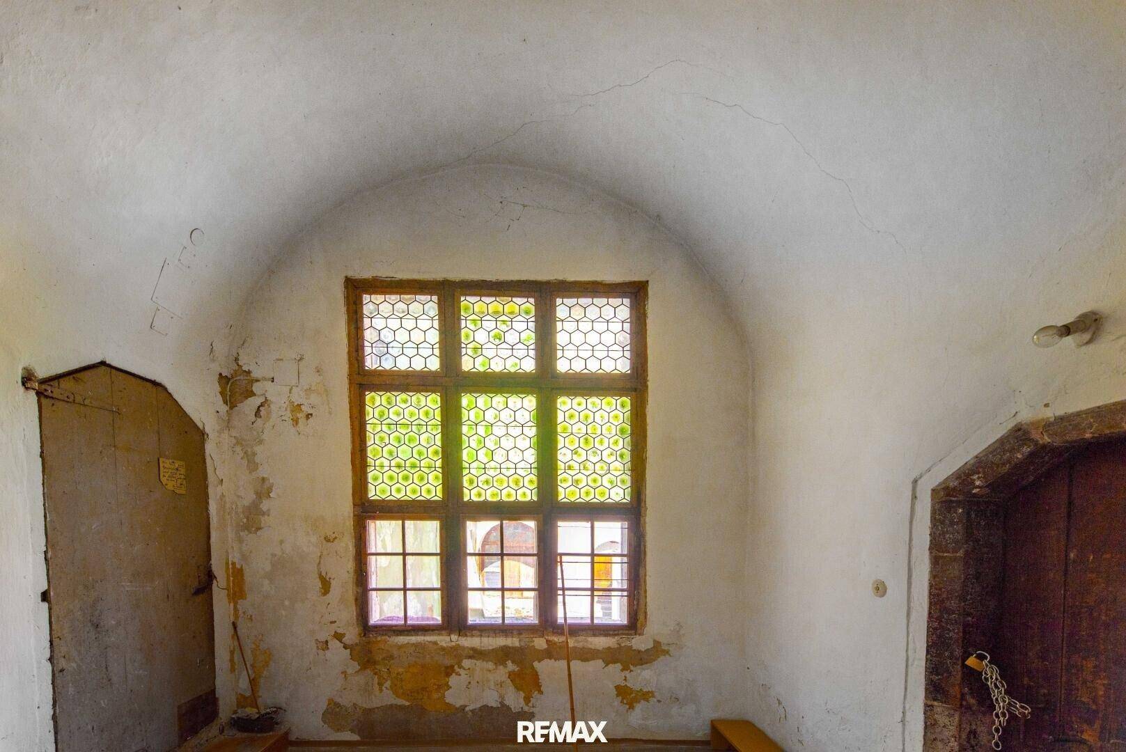 Historischer Raum mit Gewölbedecke und einem einzigartigen Fenster mit Wabenmuster, renovierungsbedürftig.