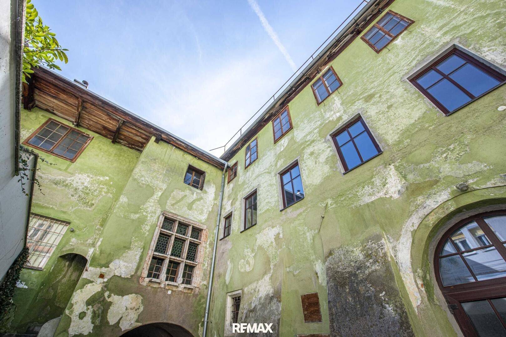 Alter Innenhof mit verputzten Wänden und historischen Fenstern, die den Charme des Gebäudes unterstreichen.