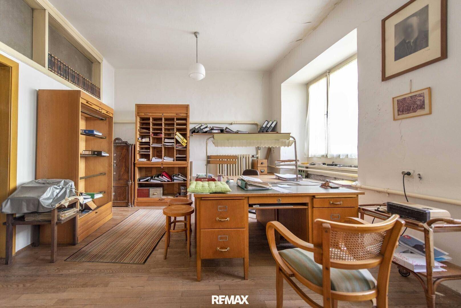 Geräumiges Büro mit Holzmöbeln, einem großen Schreibtisch und viel Tageslicht durch die Fenster.