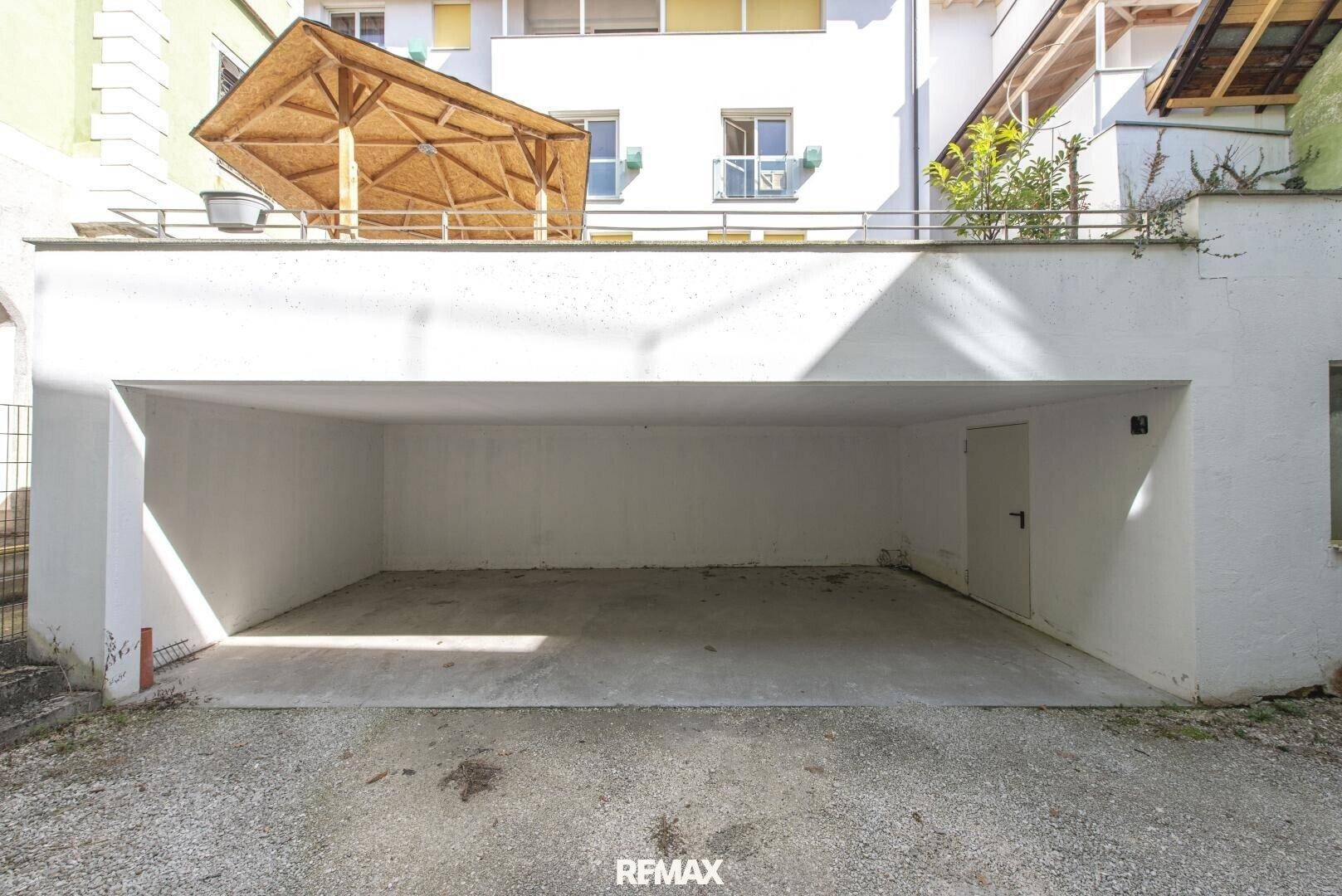 Leere Garage mit Betonboden und einem kleinen Vordach im Hintergrund.