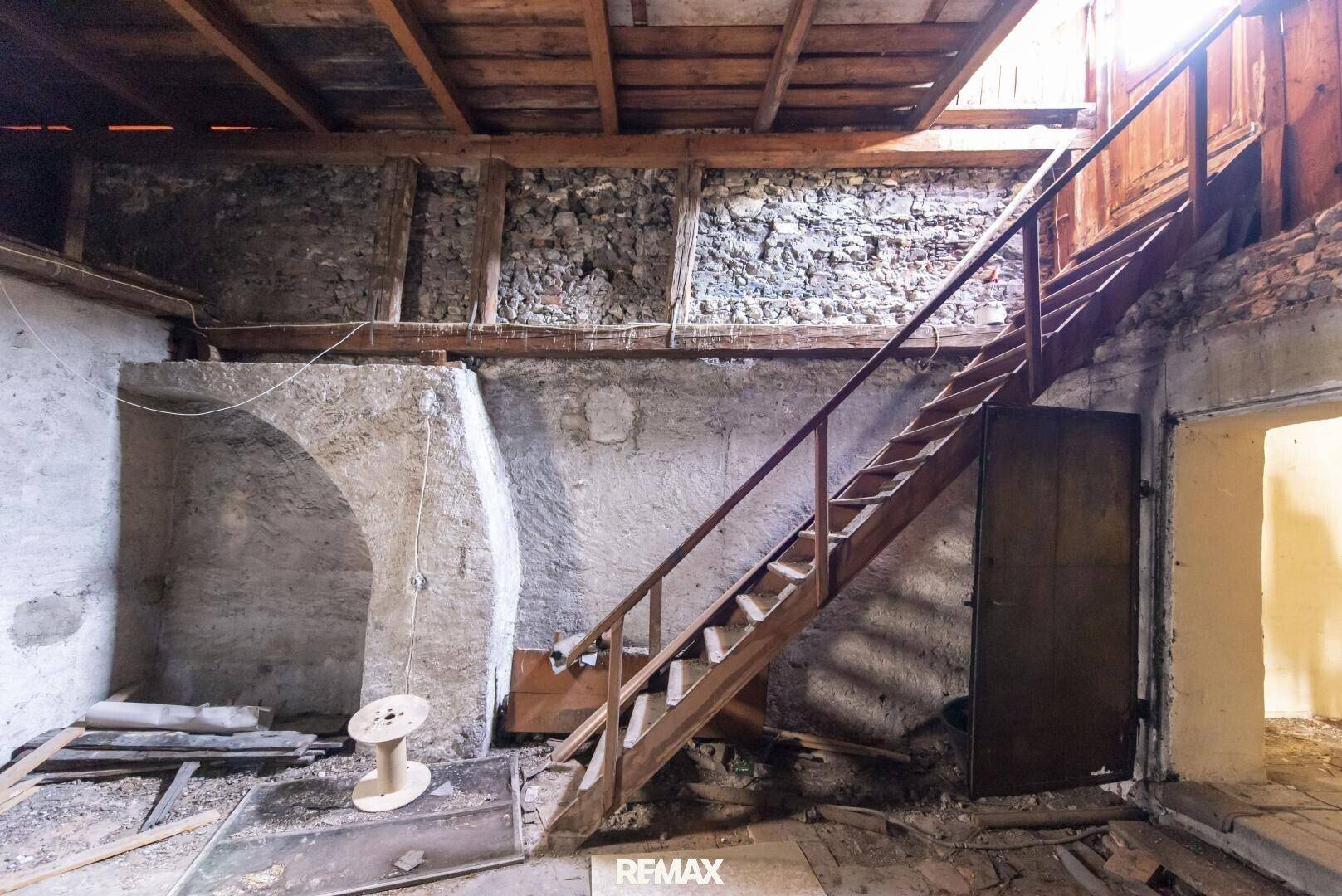 Dachboden mit sichtbaren Holzbalken und einer Holztreppe, die zu einem weiteren Bereich führt.