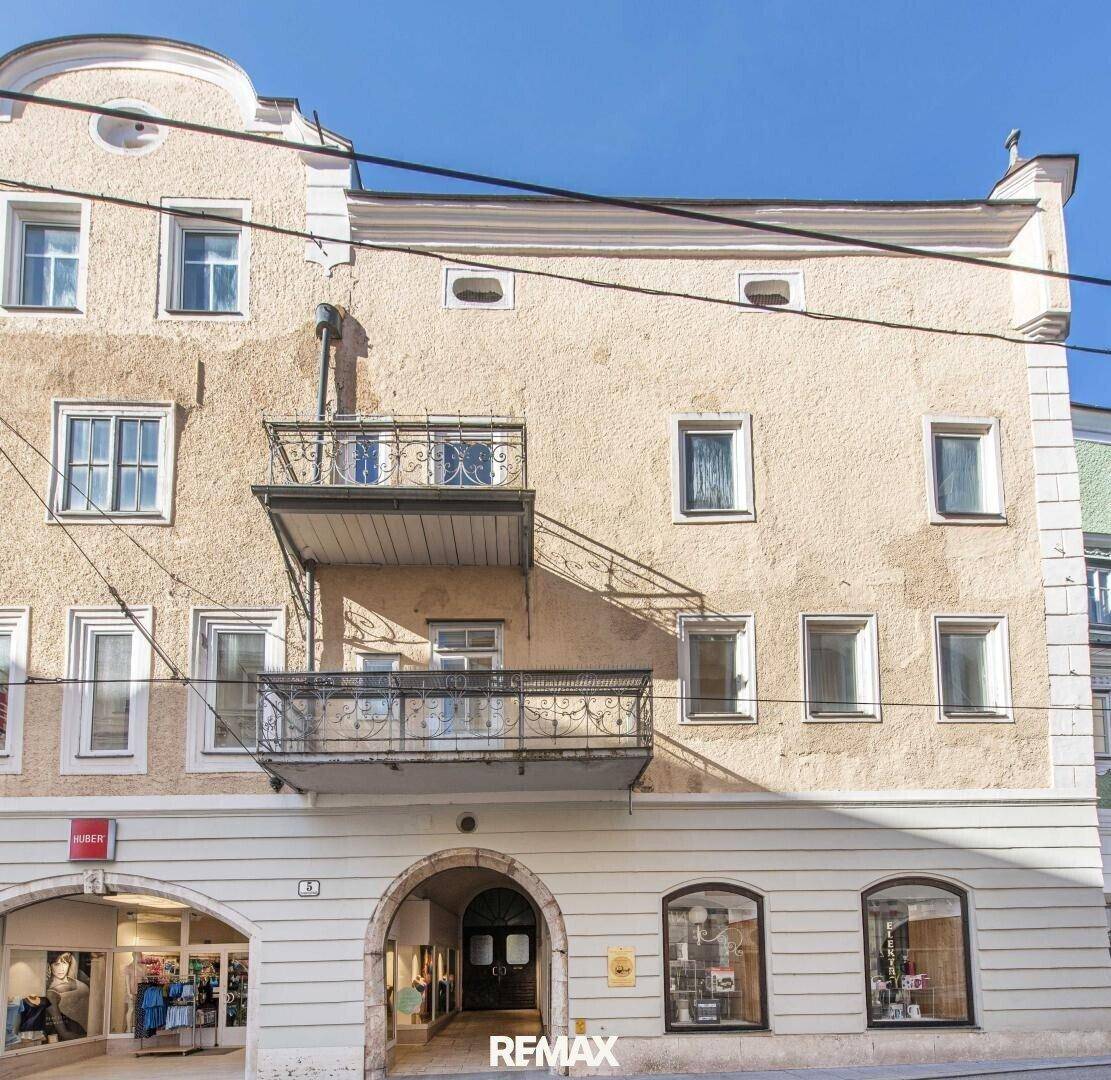 Fassade eines historischen Gebäudes mit zwei Balkonen und Geschäften im Erdgeschoss unter blauem Himmel.