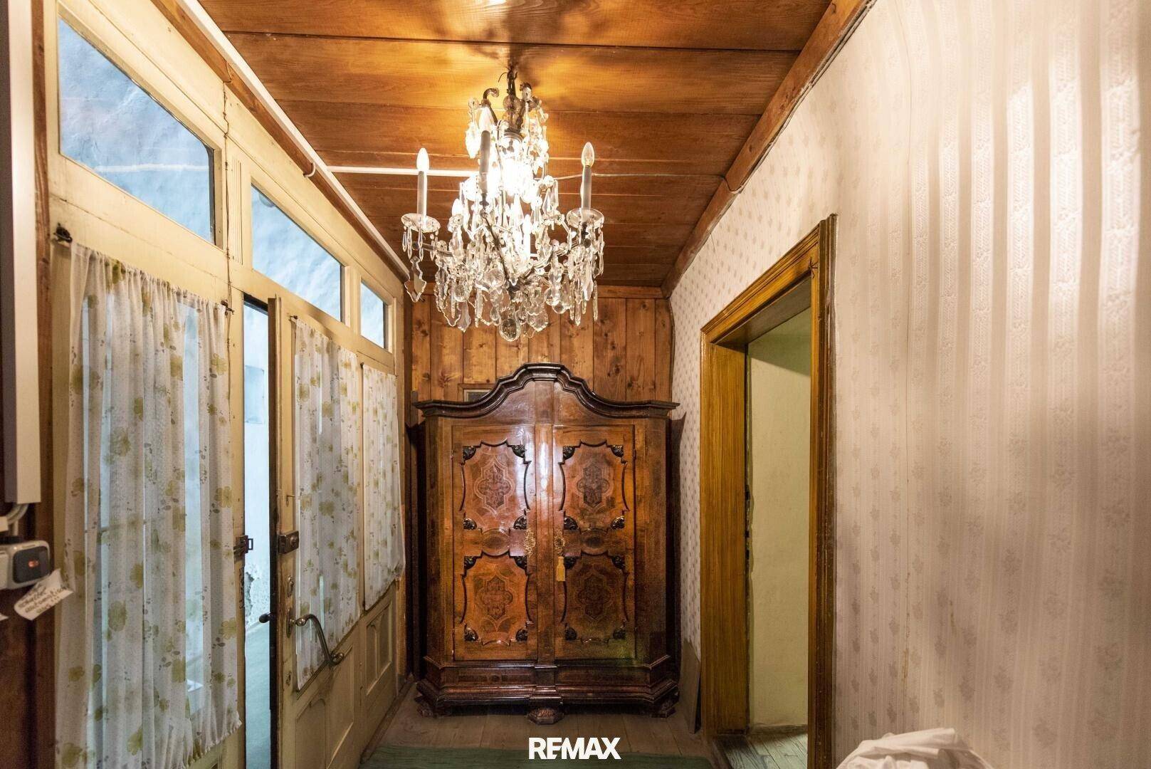 Alter Flur mit Holzvertäfelung, einem antiken Schrank und einem Kronleuchter, der eine historische Atmosphäre schafft.