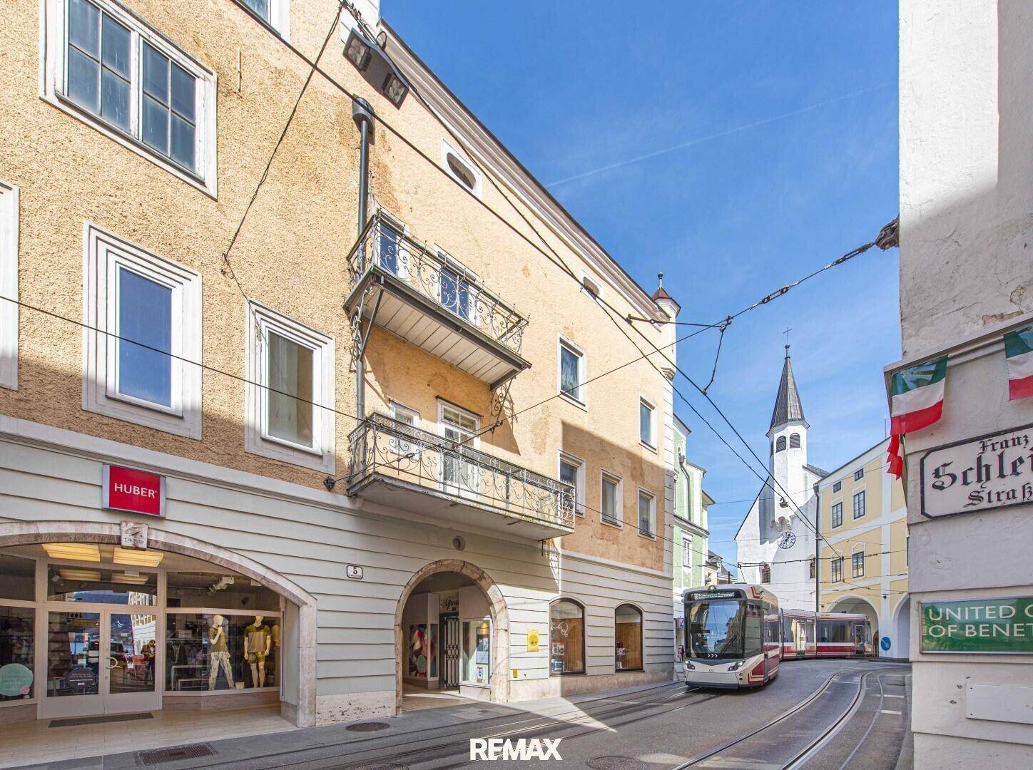 Historische Gebäude entlang einer belebten Straße mit Straßenbahn und Geschäften im Erdgeschoss.