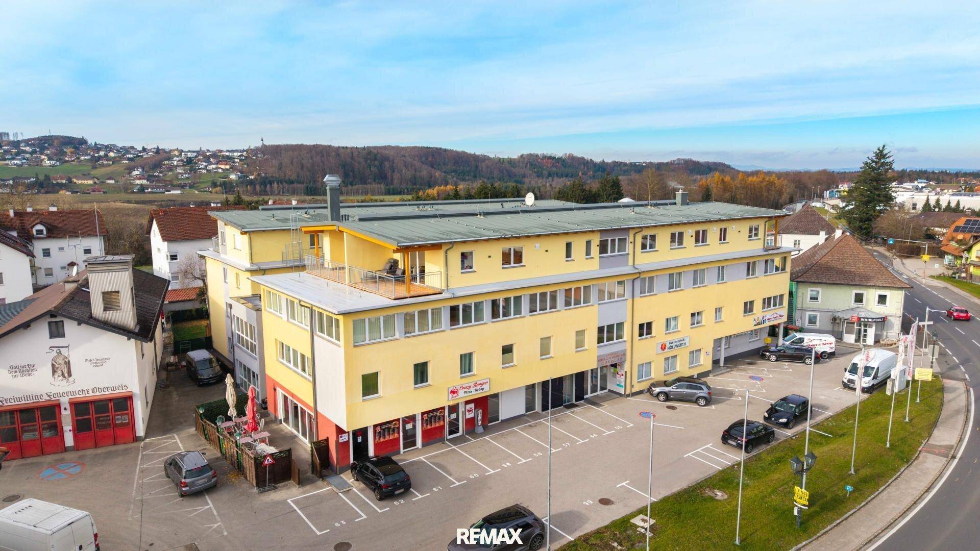 Luftaufnahme eines modernen Mehrzweckgebäudes mit Wohnungen, Geschäften und Parkplätzen in städtischer Umgebung.