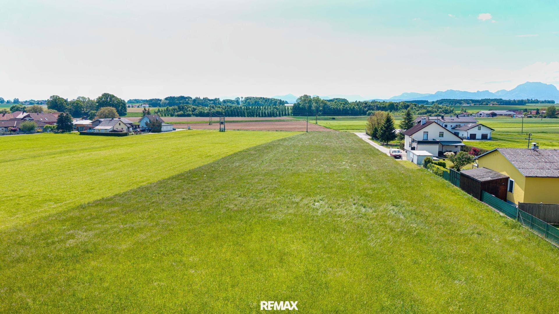 Großes grünes Grundstück mit ländlicher Bebauung und Bergen am Horizont unter weitem Himmel.