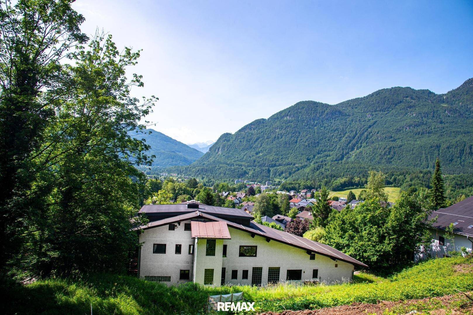 Blick auf ein Wohnhaus in ländlicher Umgebung mit majestätischem Bergpanorama im Hintergrund.
