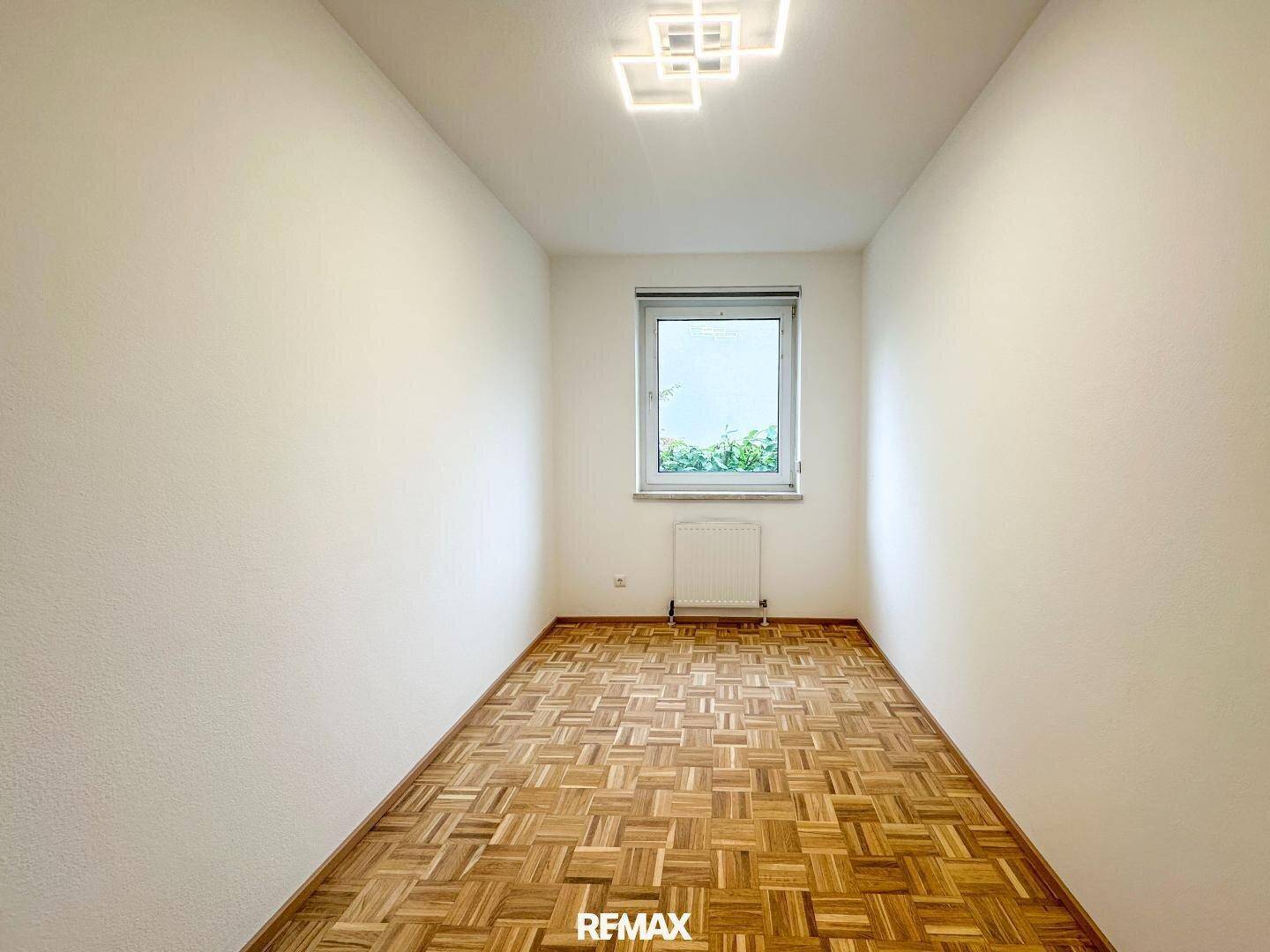 Kleines, helles Zimmer mit Parkettboden, weißen Wänden und einem Fenster.