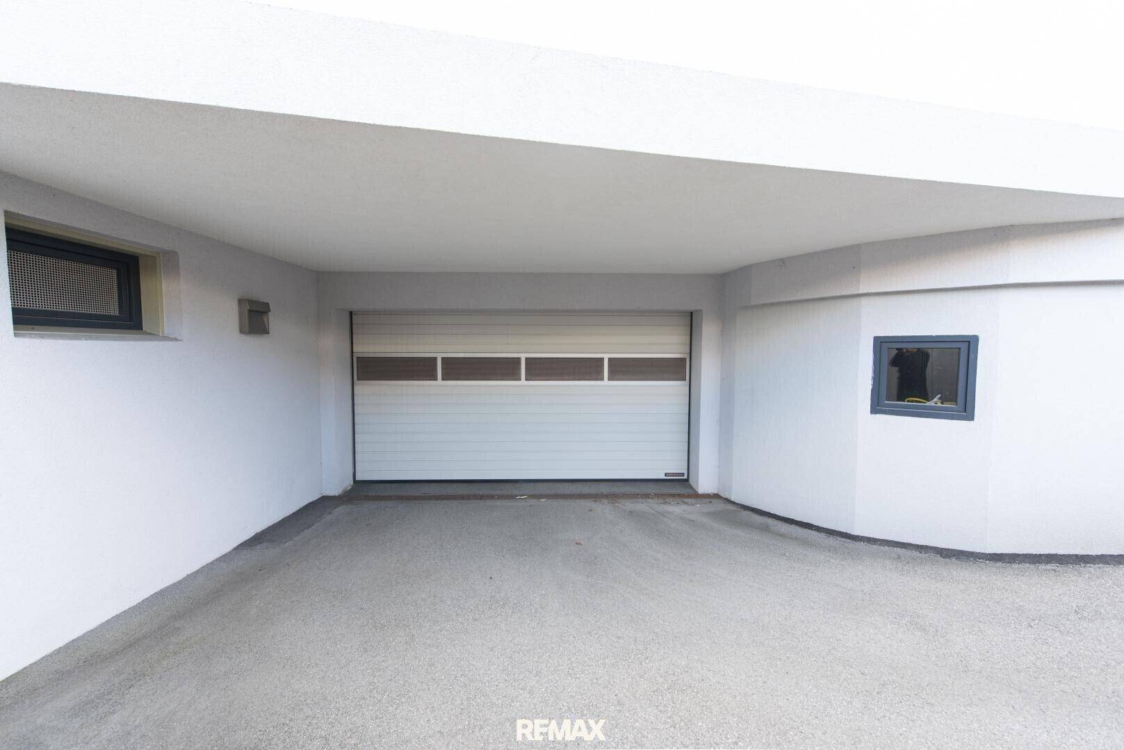 Einfahrt zu einer modernen Garage mit weißem Sektionaltor und sauberem Betonboden.