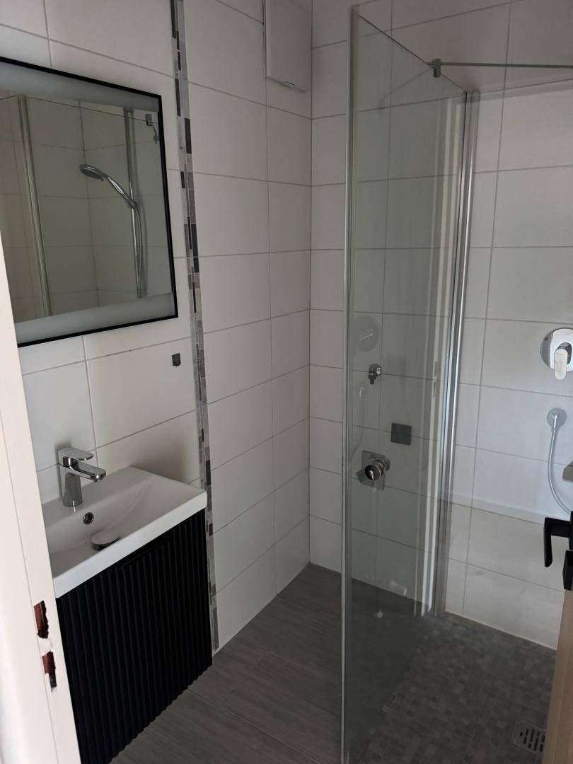 Modernes Badezimmer mit weiß gefliesten Wänden, begehbarer Dusche und einem einzelnen Waschbecken.