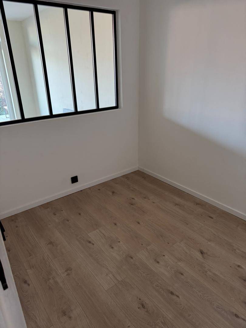 Heller, leerer Raum mit modernem Laminatboden und einem Fenster mit schwarzem Rahmen.