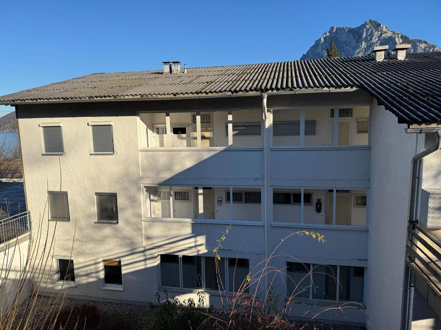 Fassade eines Wohngebäudes mit mehreren Balkonen und Fenstern, umgeben von einer natürlichen Landschaft.