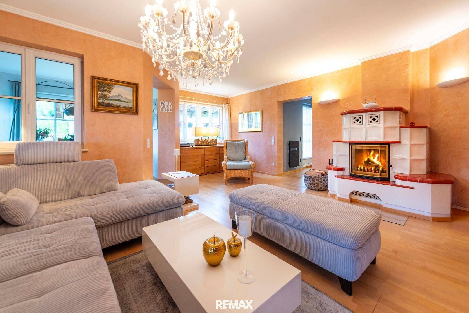 Gemütliches Wohnzimmer mit großem Sofa, Kronleuchter und einem traditionellen Kachelofen.
