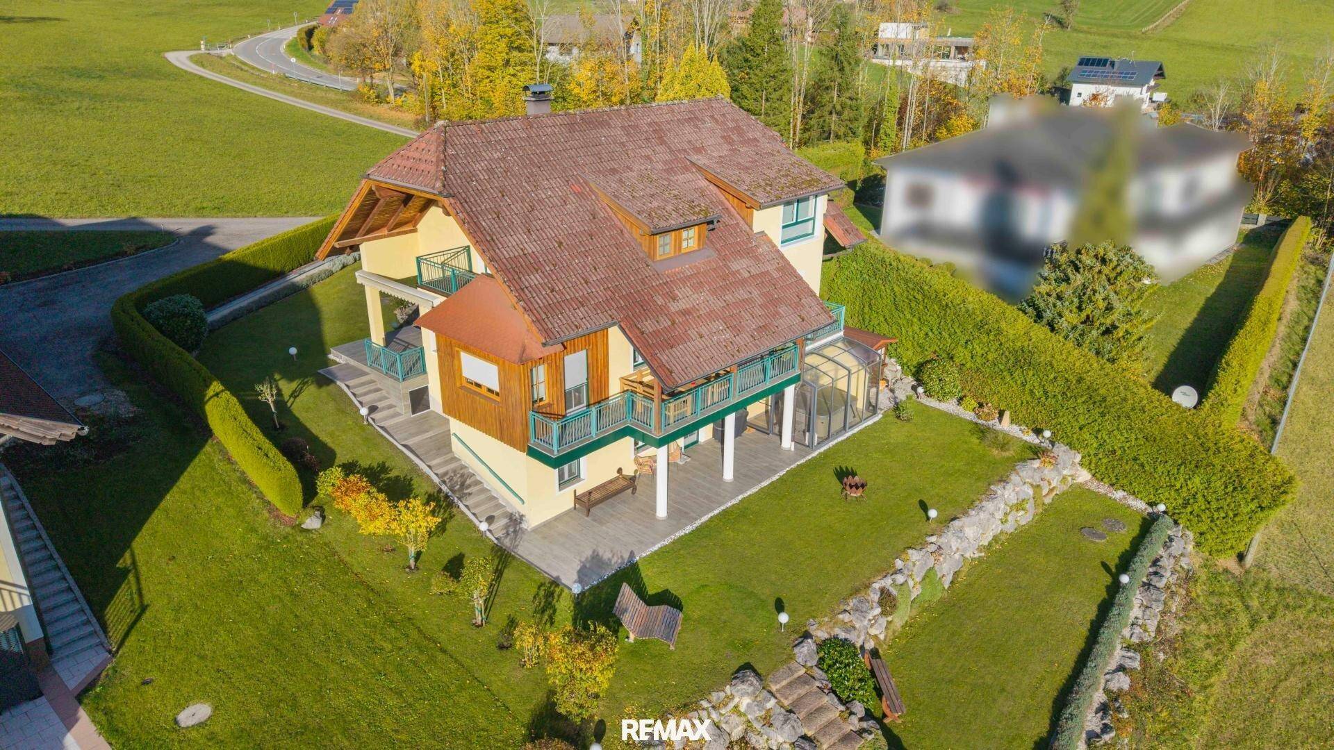 Luftaufnahme eines traditionellen Hauses mit rotem Dach, umgeben von einem gepflegten Garten und grünen Hügeln.