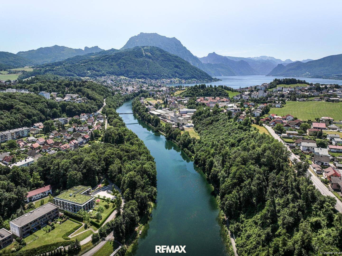 Luftaufnahme einer Stadt am Fluss mit See- und Bergblick in der Ferne.