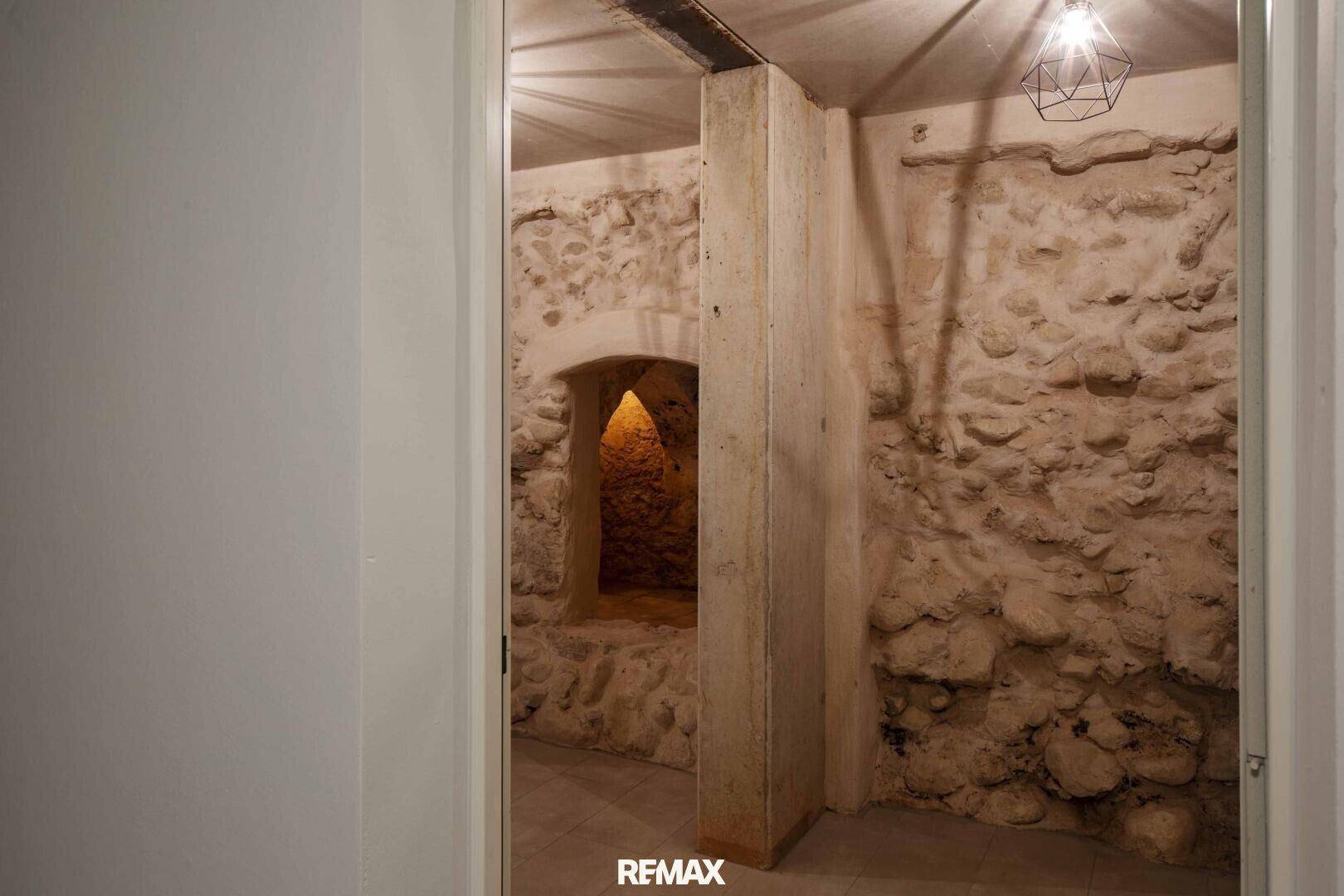 Rustikaler Kellerraum mit freiliegenden Steinmauern und einer kleinen Nische, beleuchtet von einer modernen Lampe.