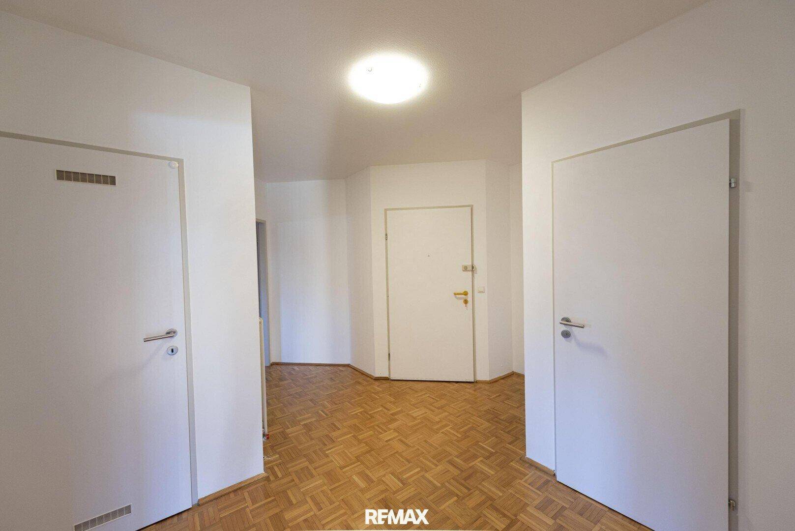 Heller Flur mit gut erhaltenem Parkettboden und mehreren weißen Türen, ausgestattet mit einer Deckenleuchte.