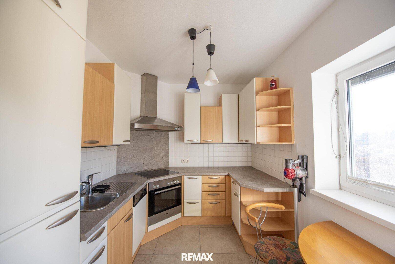 Funktionale Küche mit hellen Holz- und weißen Schränken, ausgestattet mit Backofen und Dunstabzugshaube.