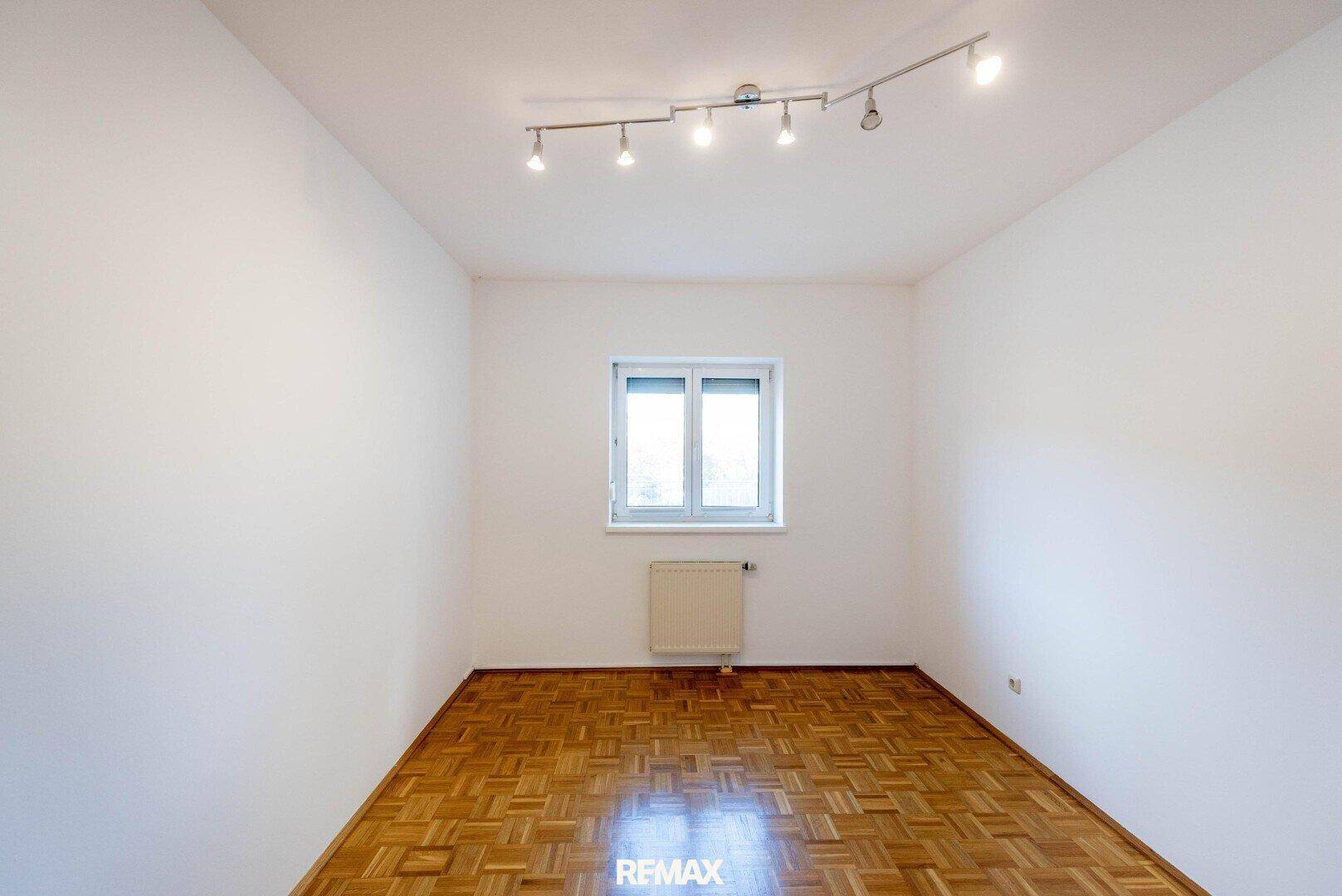 Helles Zimmer mit Parkettboden, einem Fenster und einer praktischen Deckenbeleuchtung.