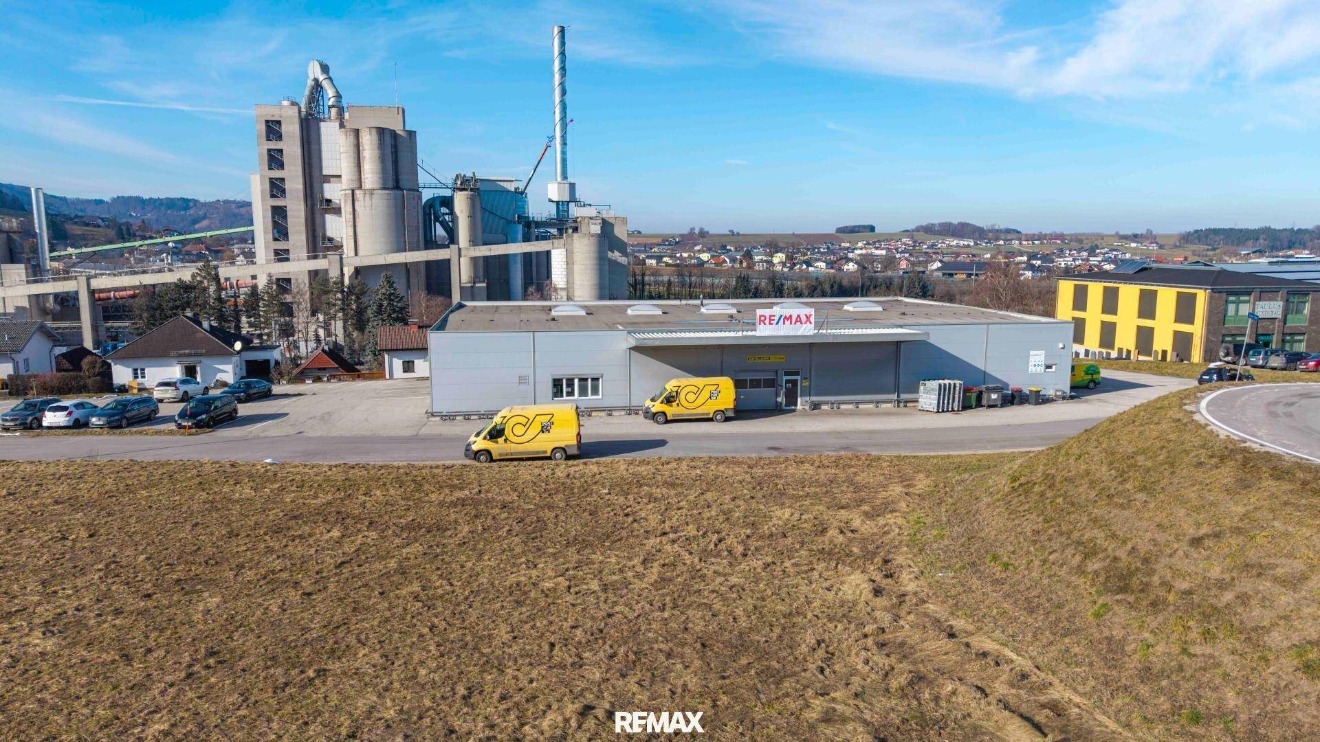 Weitläufige Außenansicht mit Gewerbegebäuden, einem Feld und industrieller Architektur im Hintergrund.