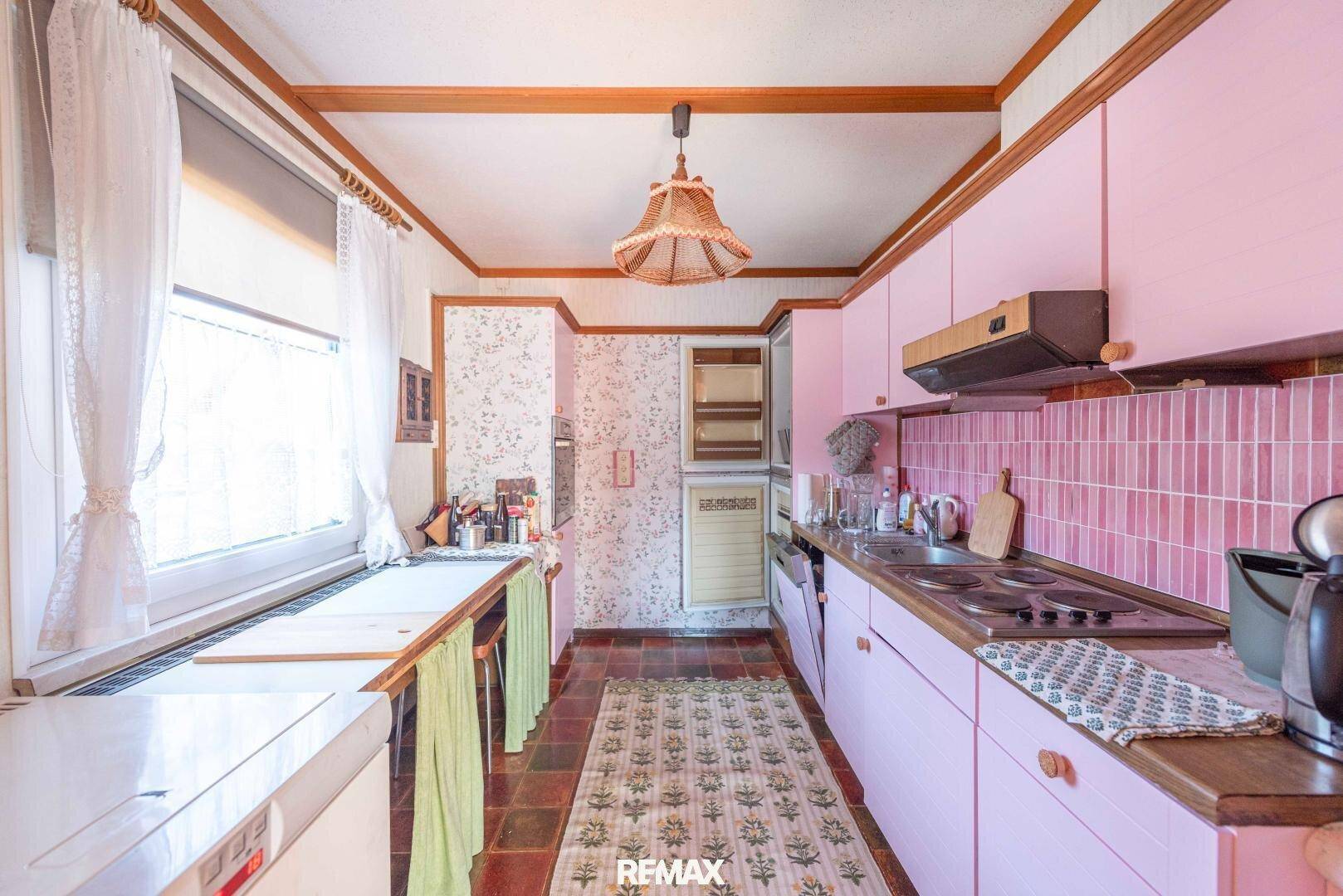 Küche im Retro-Stil mit rosa Schränken, Holztheke und einem großen Fenster für Tageslicht.