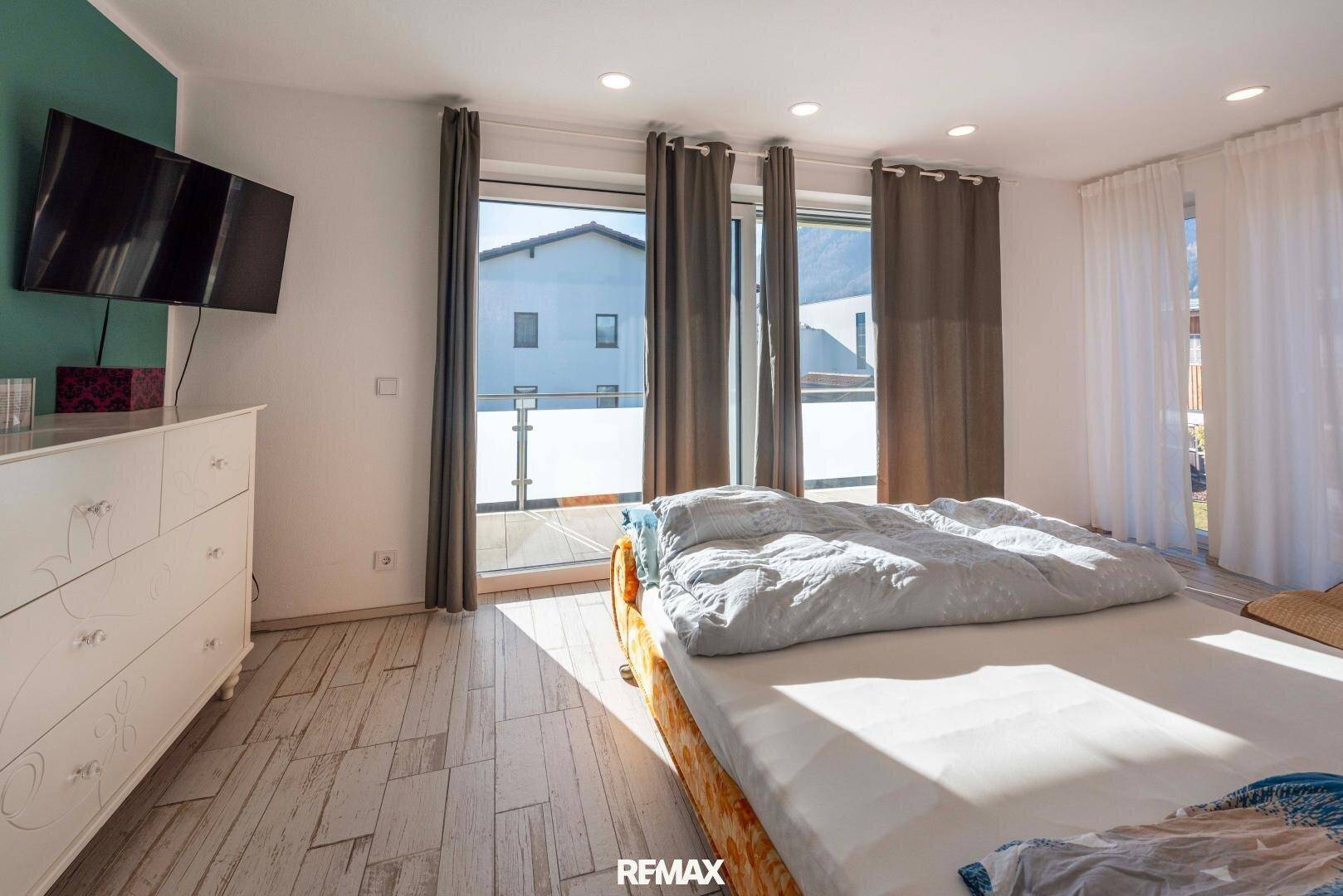 Geräumiges Schlafzimmer mit Doppelbett und großen Fenstern, die Zugang zu einem Balkon bieten.