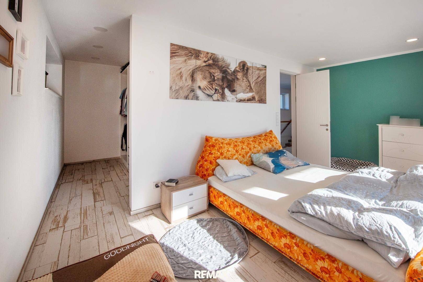 Hauptschlafzimmer mit Doppelbett und offenem begehbarem Kleiderschrankbereich, hell und modern gestaltet.