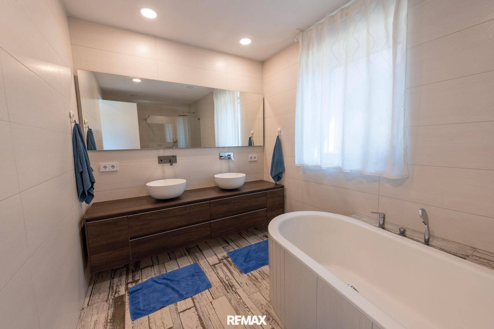 Modernes Badezimmer mit freistehender Badewanne, Doppelwaschbecken und großem Spiegel.