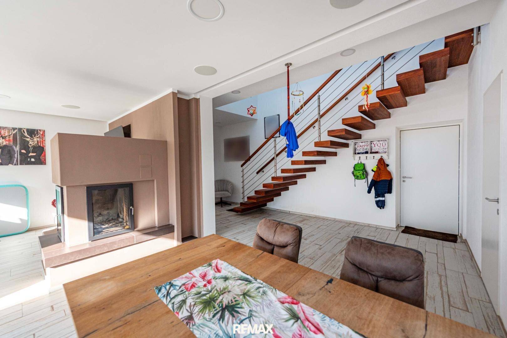 Offener Wohn- und Essbereich mit Holztisch, Kamin und Zugang zur modernen Holztreppe.