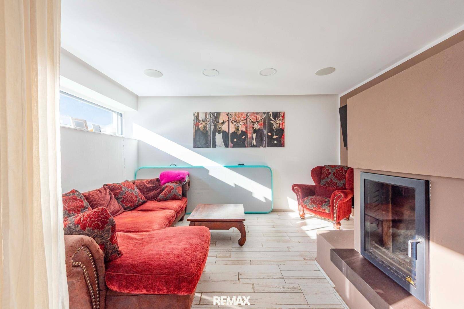 Gemütliches Wohnzimmer mit rotem Sofa, Kamin und hellem Fliesenboden, ideal zum Entspannen.