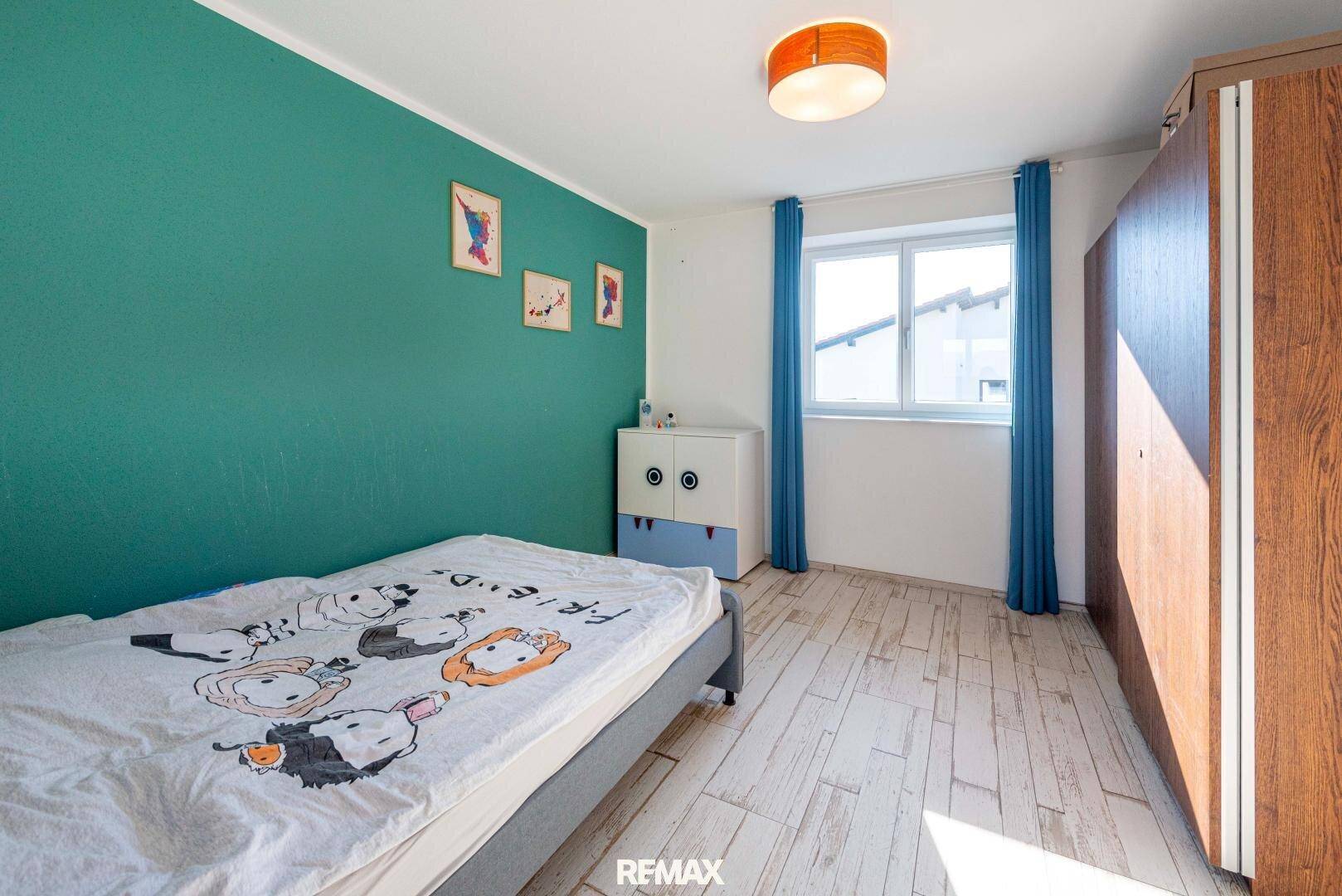 Helles Schlafzimmer mit Einzelbett, grüner Akzentwand und Fenster, ausgestattet mit Holzschrank.